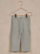 Light gray children's pants hanging on a copper hanger against a neutral background.
