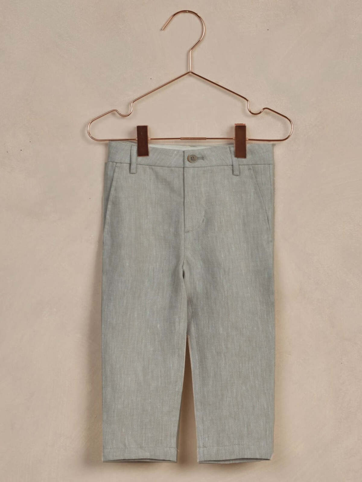 Light gray children's pants hanging on a copper hanger against a neutral background.