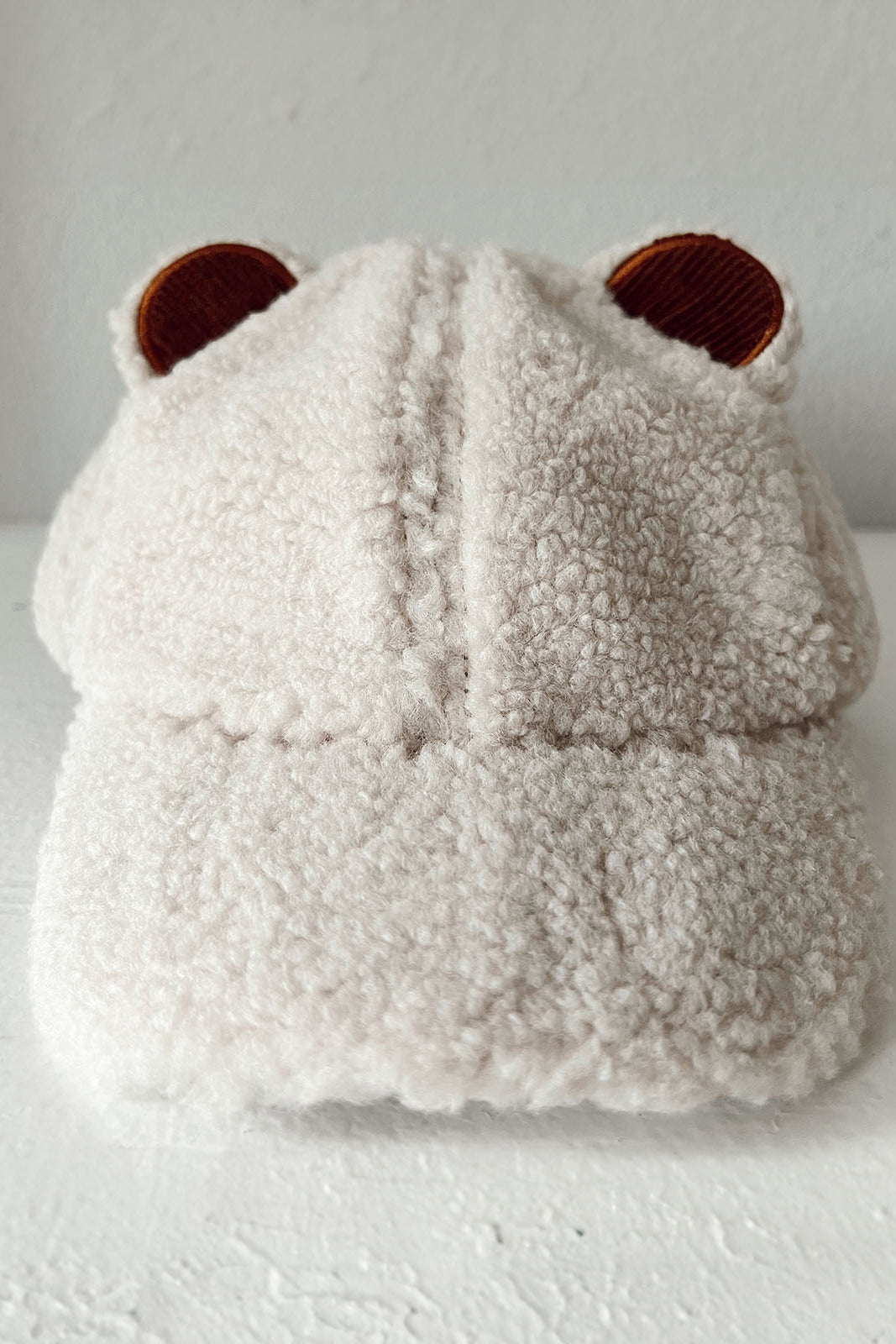 Fluffy beige cap with bear ears displayed on a white surface against a plain background.