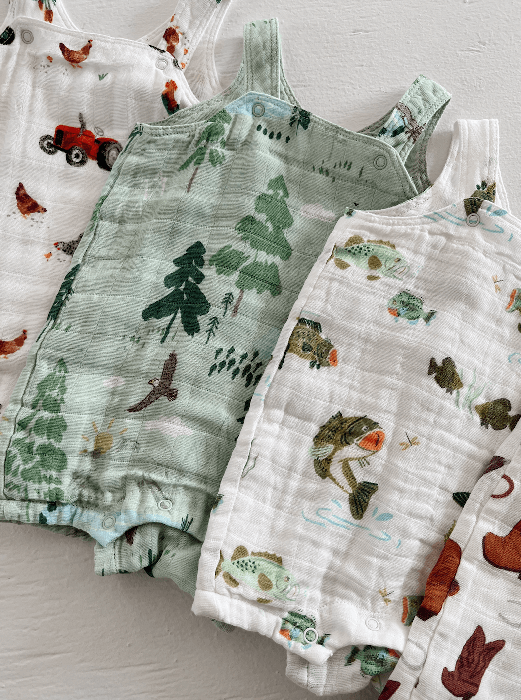 Colorful children's overalls featuring nature and farm-themed prints, arranged neatly on a light background.