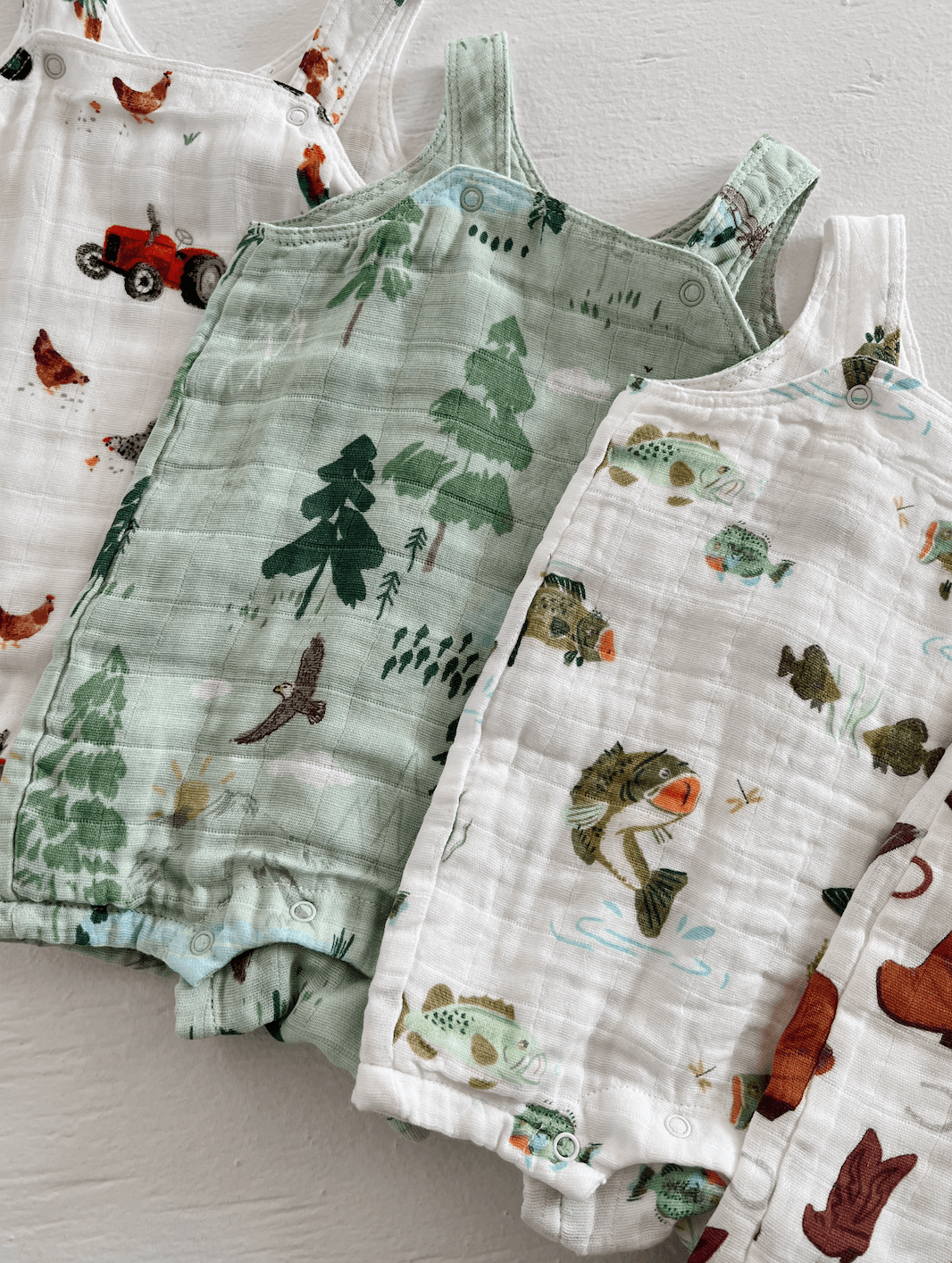 Colorful children's overalls featuring nature and farm-themed prints, arranged neatly on a light background.
