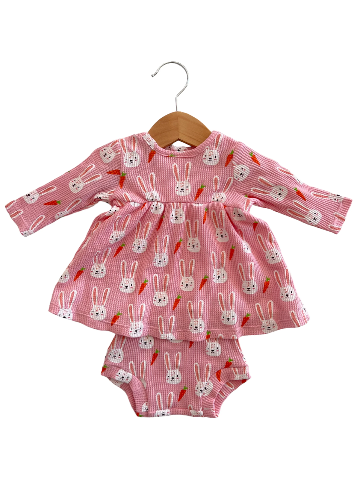 Pink dress with bunny pattern and matching shorts, displayed on a wooden hanger. Perfect for toddlers.