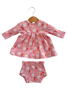 Pink dress and shorts set with bunny and carrot prints, hanging on a wooden hanger. Ideal for kids' spring fashion.