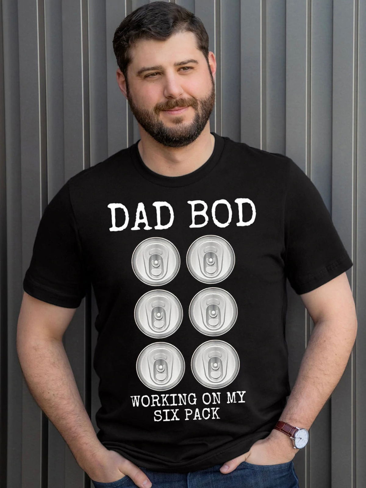 Man wearing a black t-shirt that says "Dad Bod Working on My Six Pack" with six beer cans graphic.