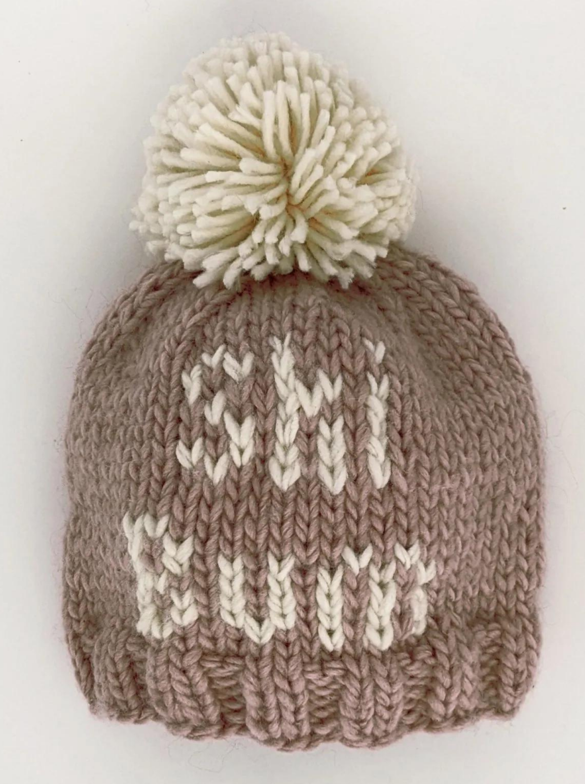 Knitted pink beanie hat with a cream pom-pom and the word "SHI" woven into the design.