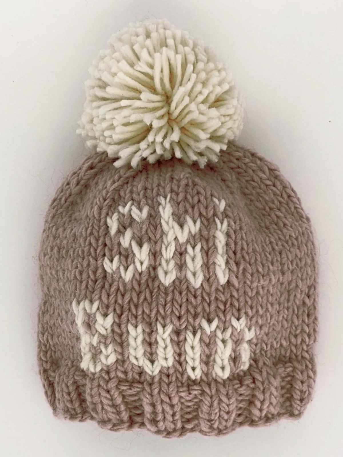 Knitted pink beanie hat with a cream pom-pom and the word "SHI" woven into the design.