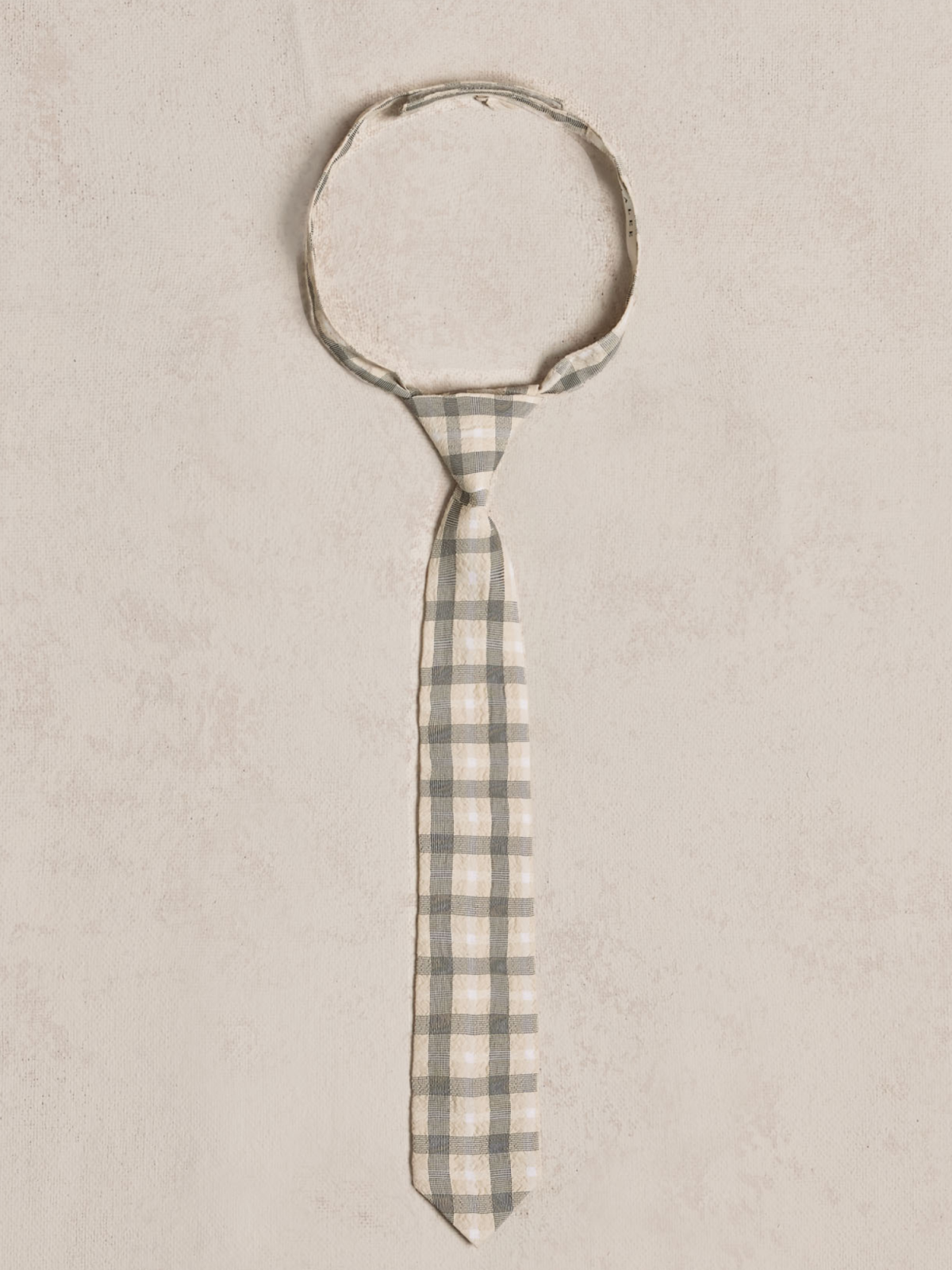 Gray and cream checkered tie laid flat on a light textured background.