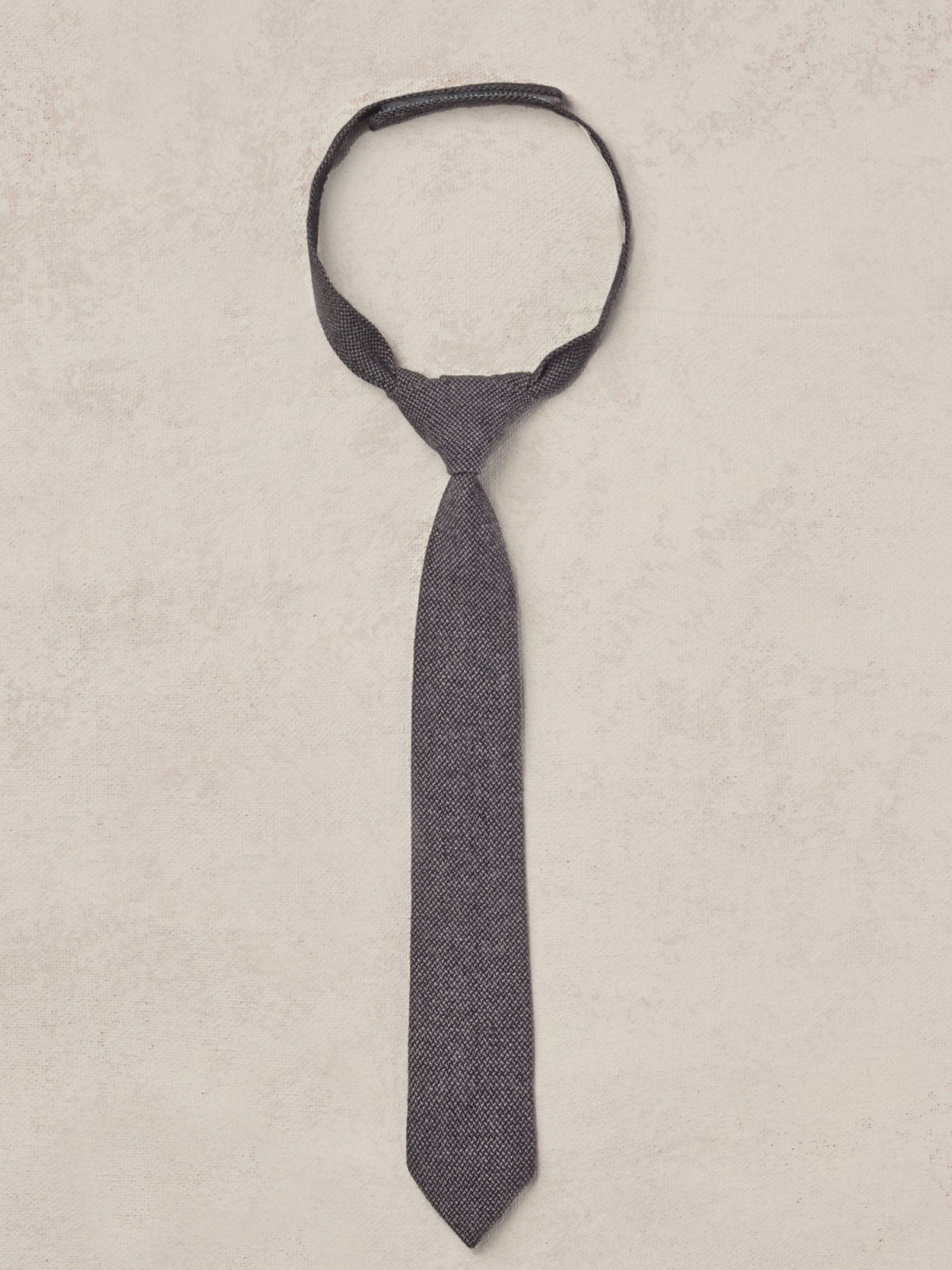 Dark patterned tie laid flat on a textured background, showcasing its length and design.