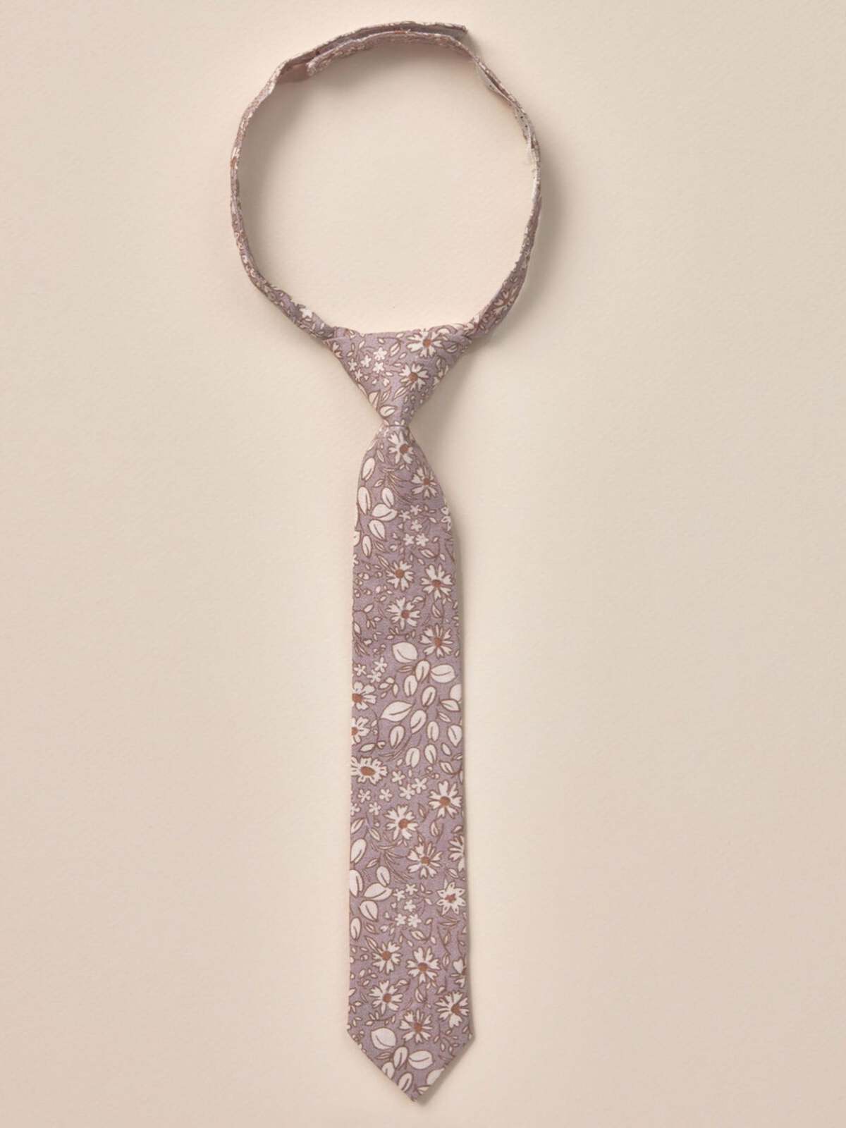 Floral patterned tie hanging against a neutral background, showcasing delicate leaves and blossoms.