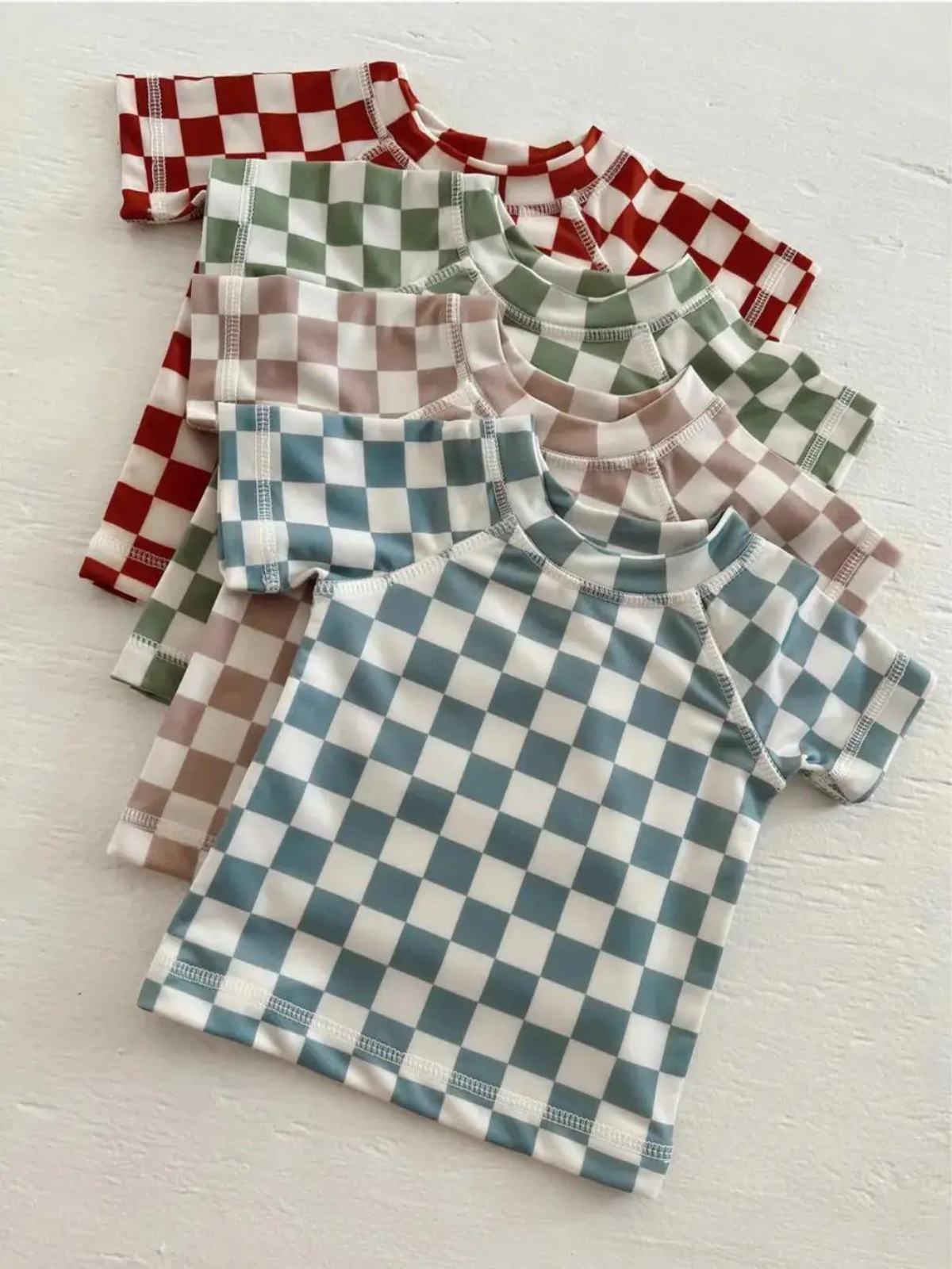 Four short-sleeve checkered shirts in various colors stacked on a white surface.