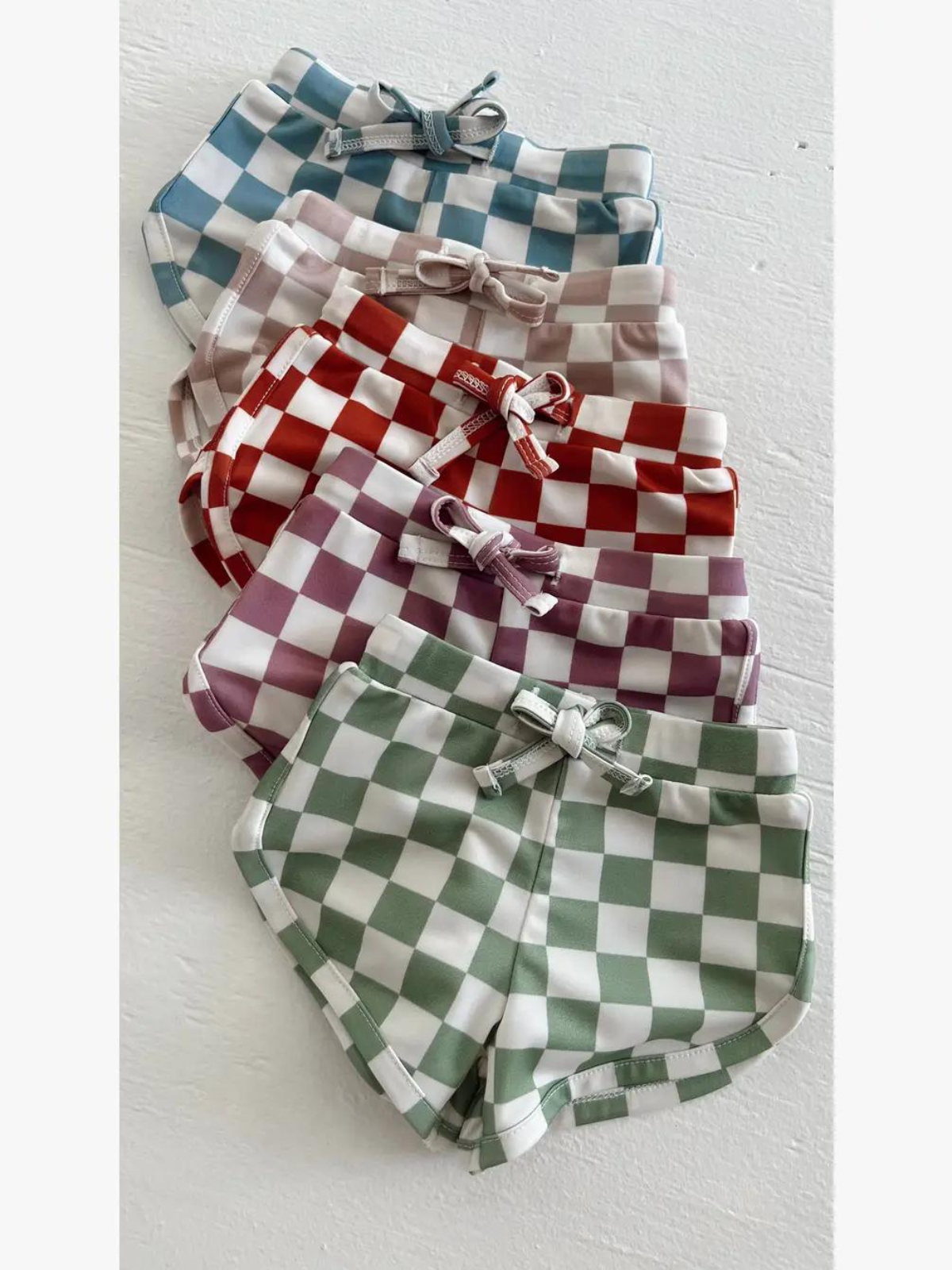 Colorful checkered swim shorts displayed in a stack, featuring green, red, blue, pink, and purple patterns.