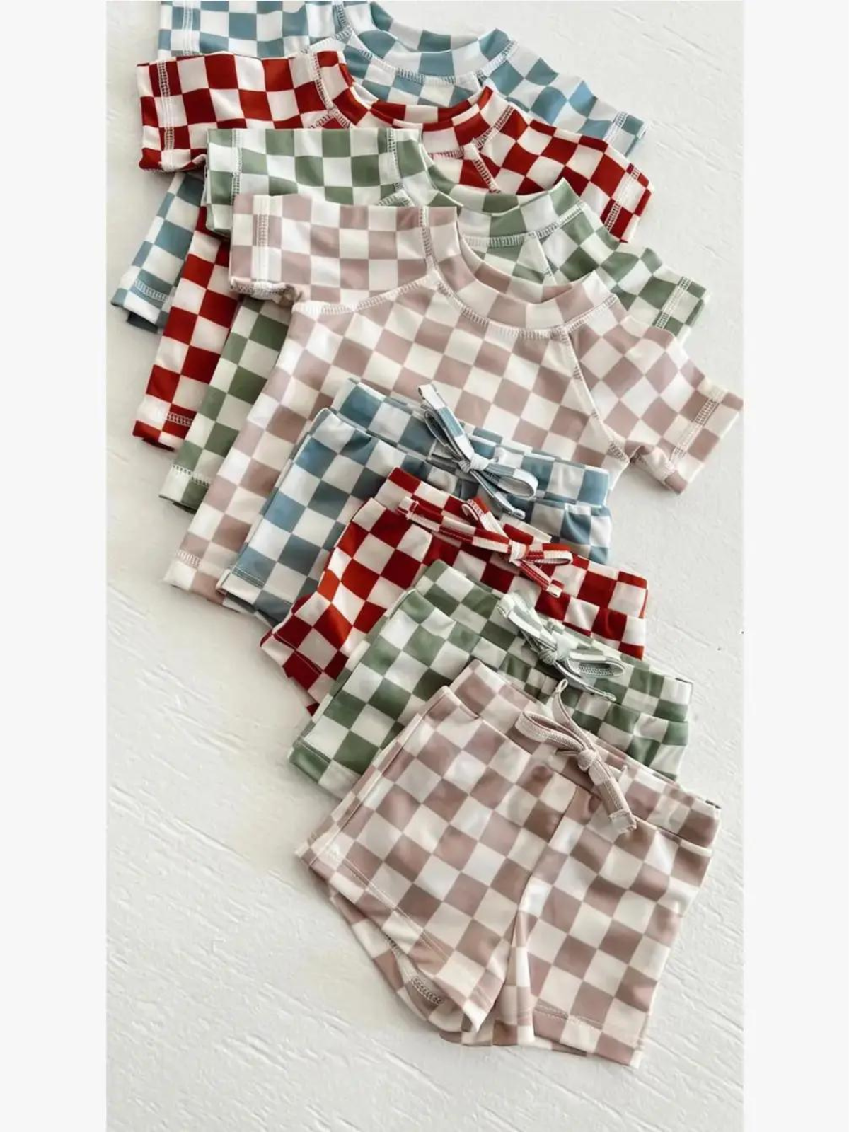 Colorful checkered baby outfits stacked neatly, including shirts and shorts in various pastel shades.