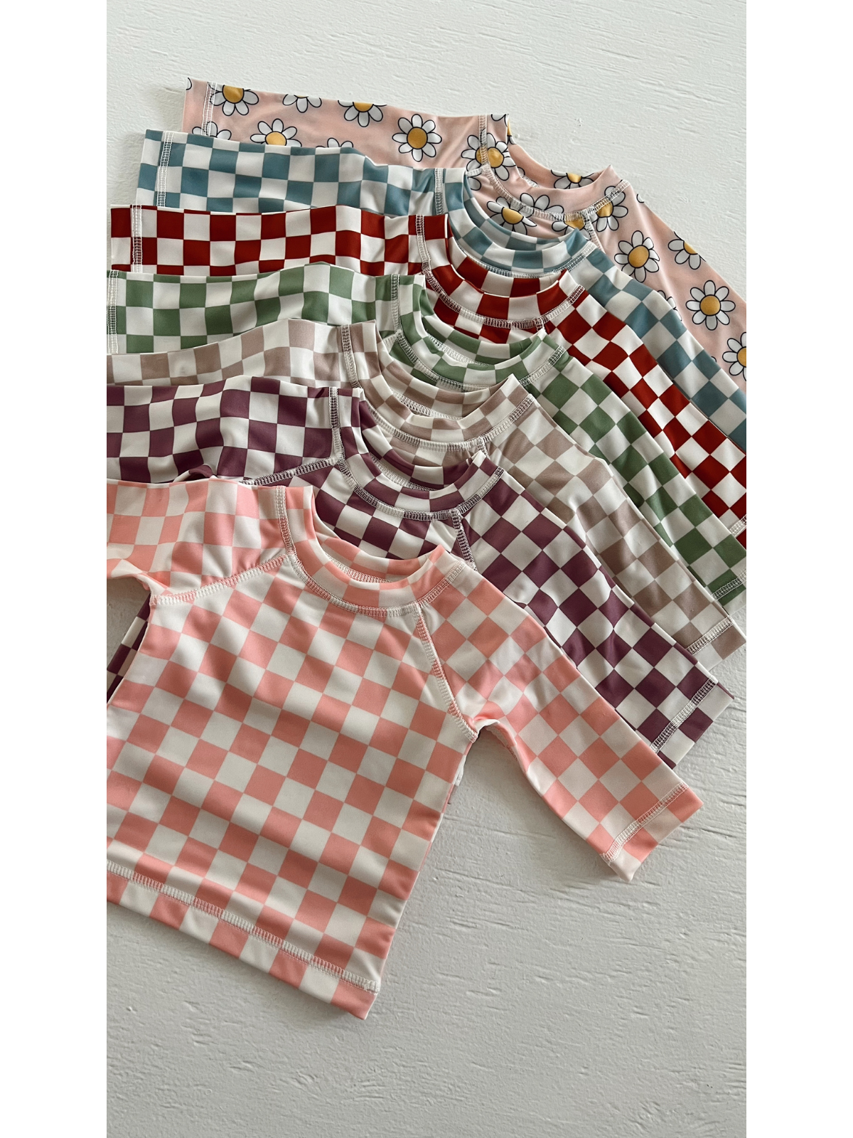 Colorful array of short-sleeve patterned shirts featuring checkered designs and floral accents on a light background.