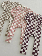 Three checkered baby onesies in brown, pink, and burgundy arranged neatly on a light background.