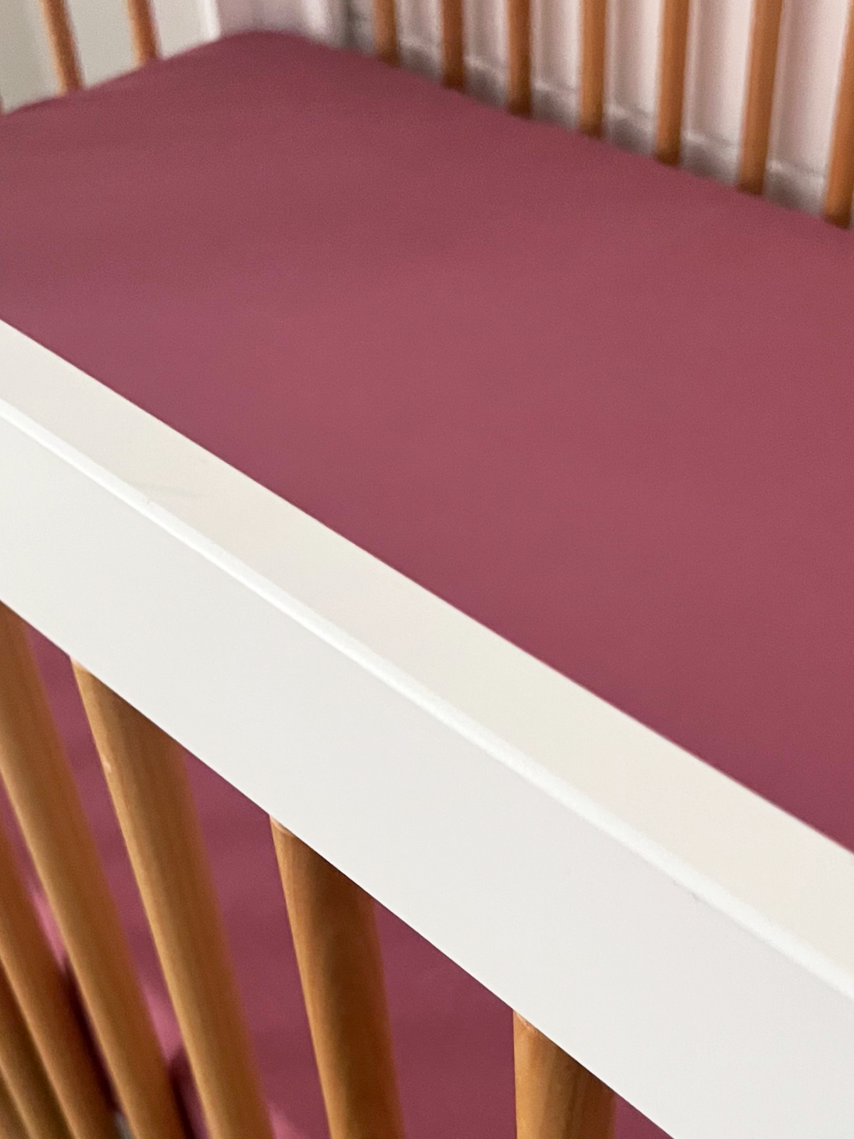 Close-up of a crib with a white frame and a pink mattress cover.