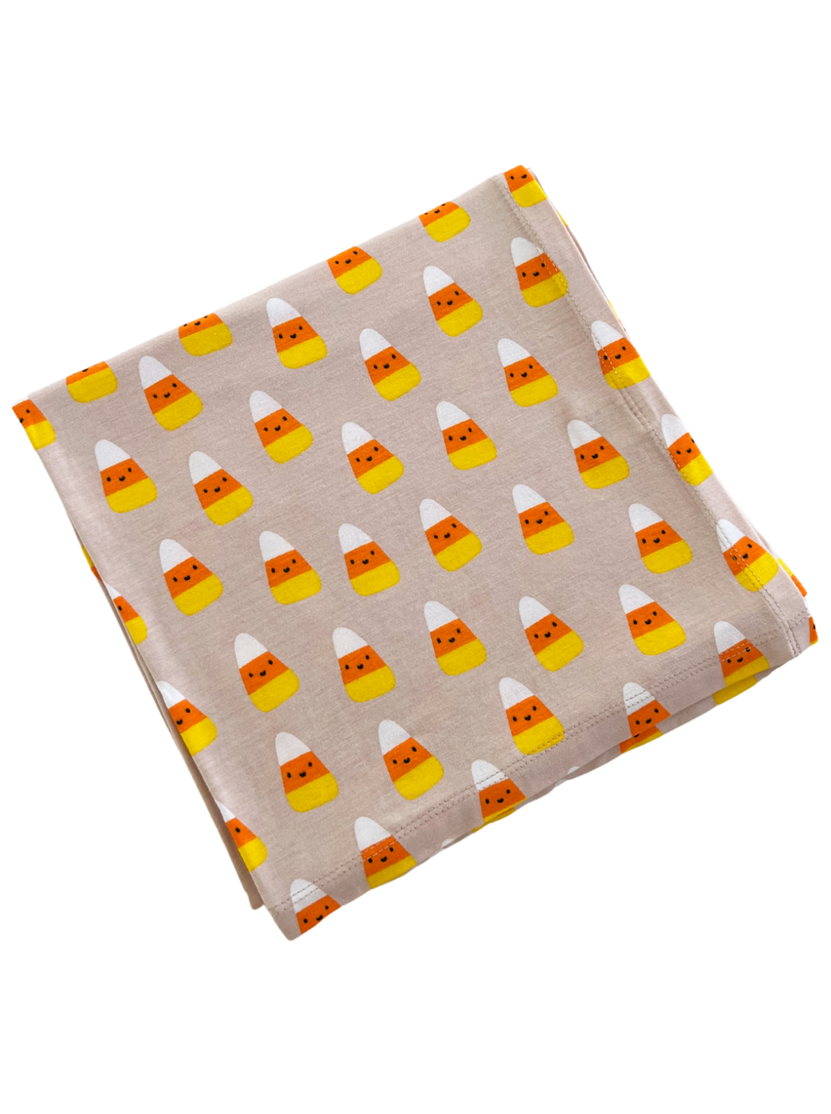 Folded fabric with a playful candy corn pattern in orange, yellow, and white on a light beige background.