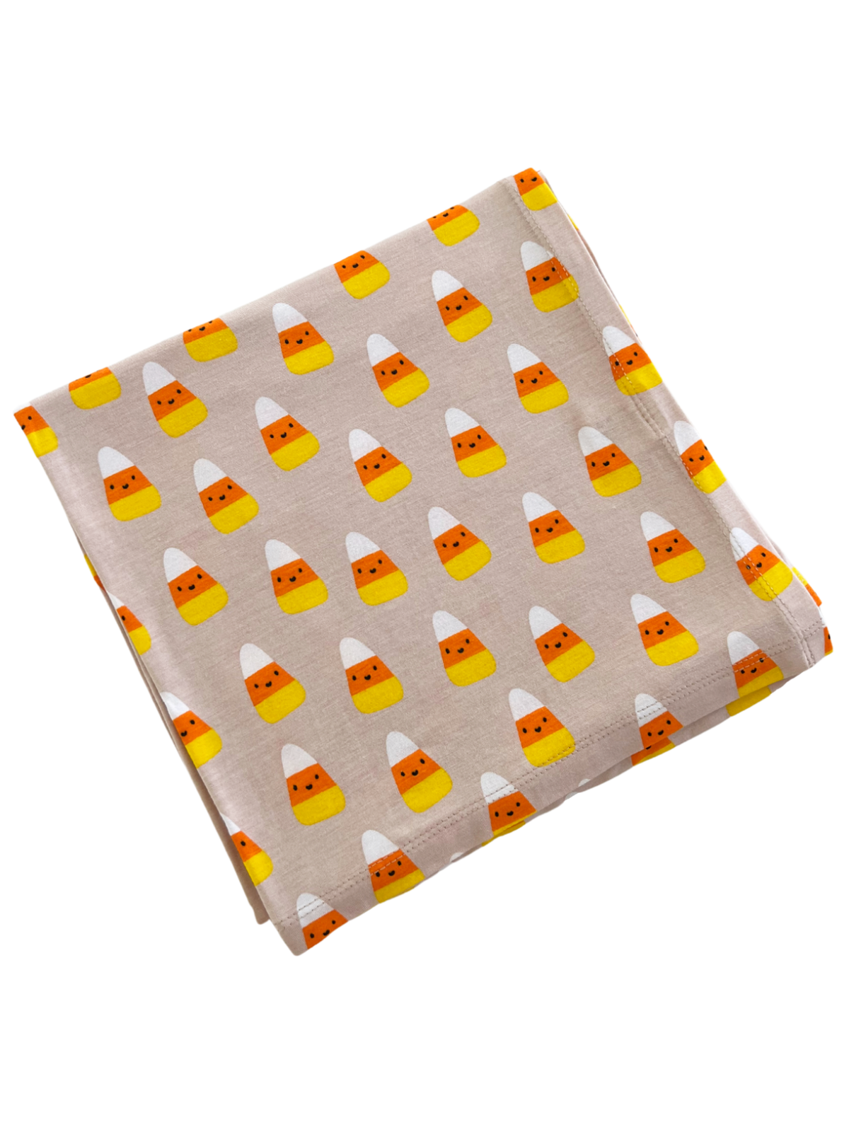 Folded fabric with a playful candy corn pattern in orange, yellow, and white on a light beige background.