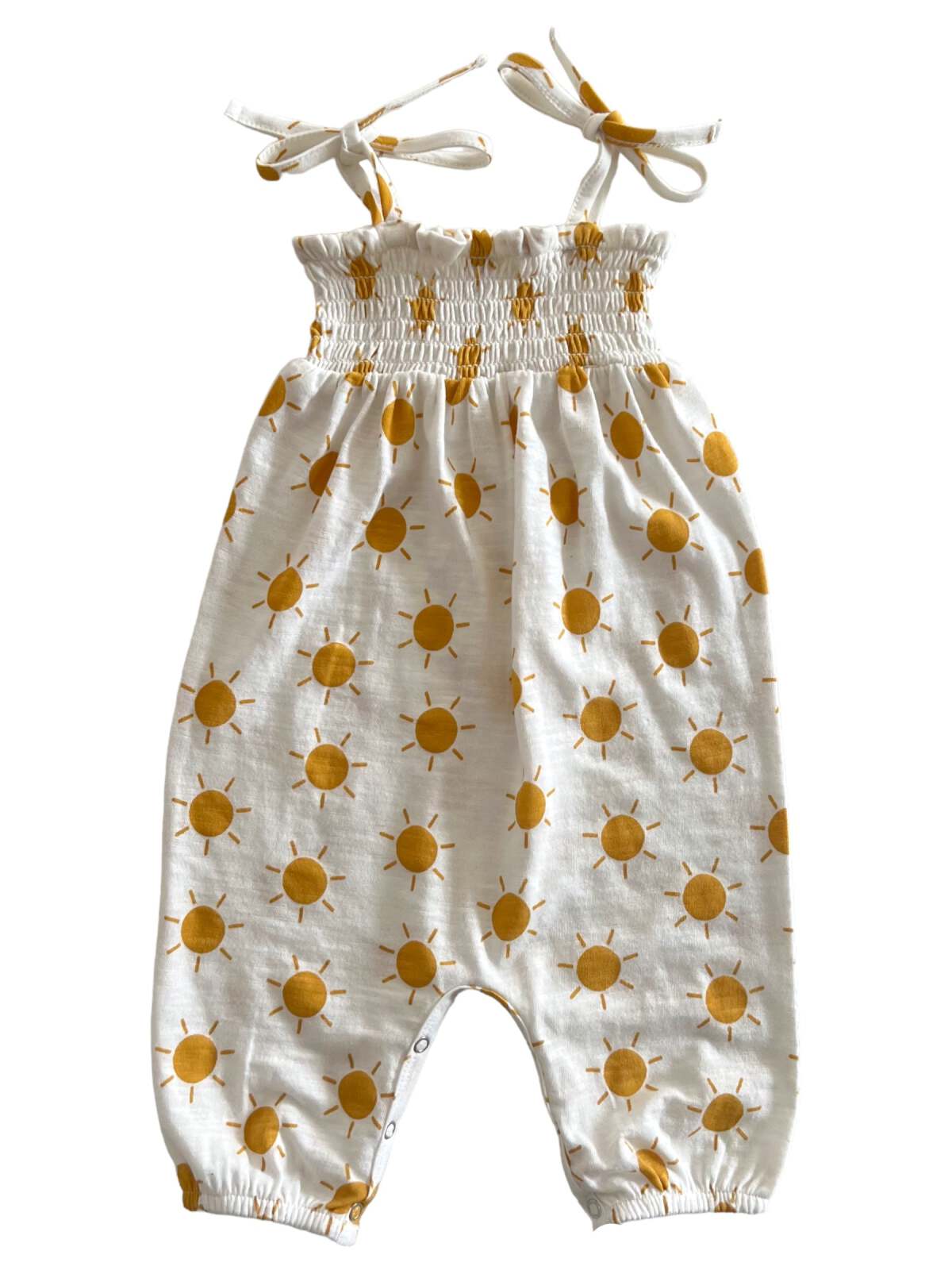 White jumpsuit with yellow sun patterns and tie straps, featuring a smocked bodice and snap closure at the bottom.