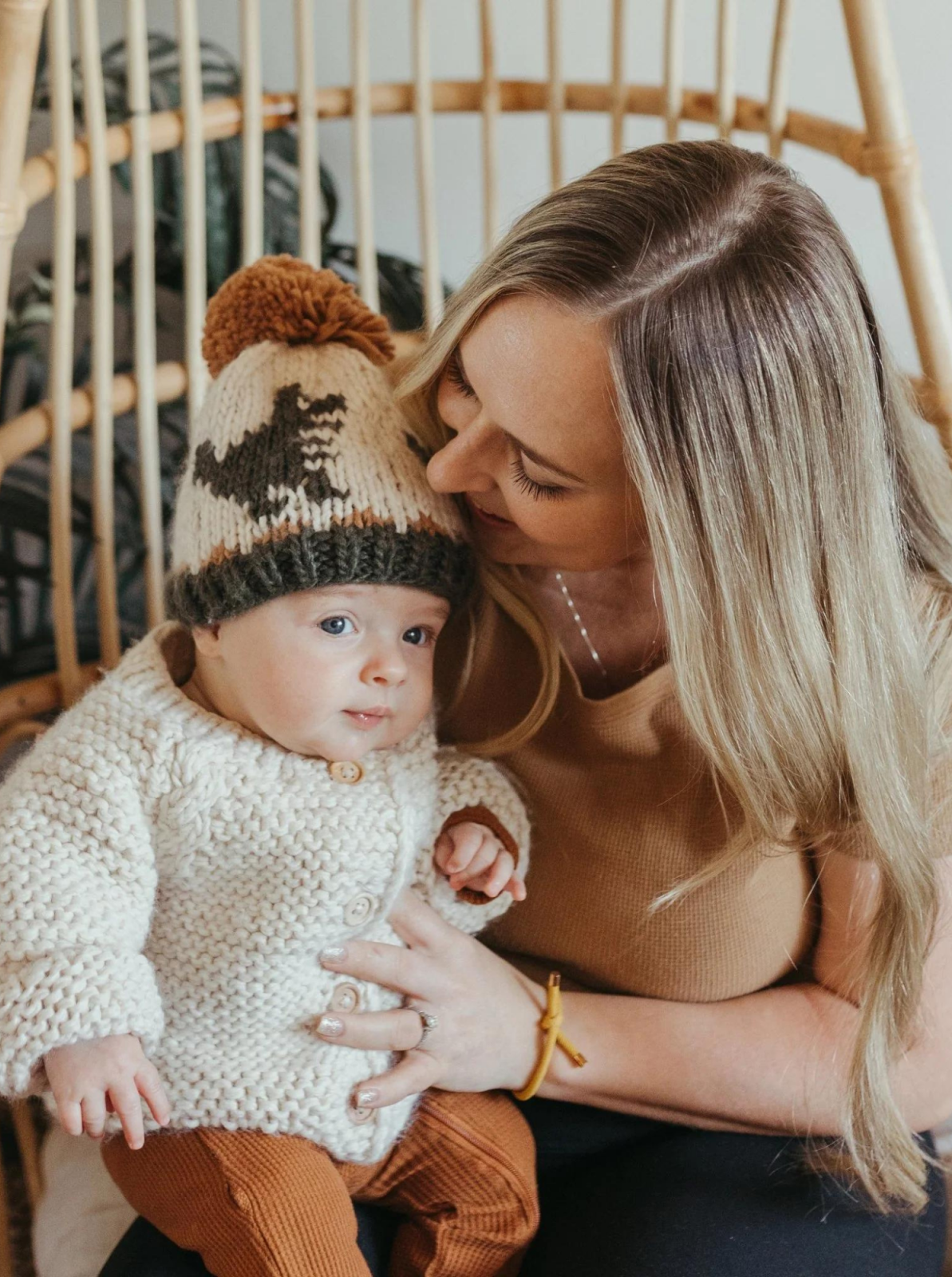 Mother and baby in cozy knitwear, smiling together in a stylish indoor setting.