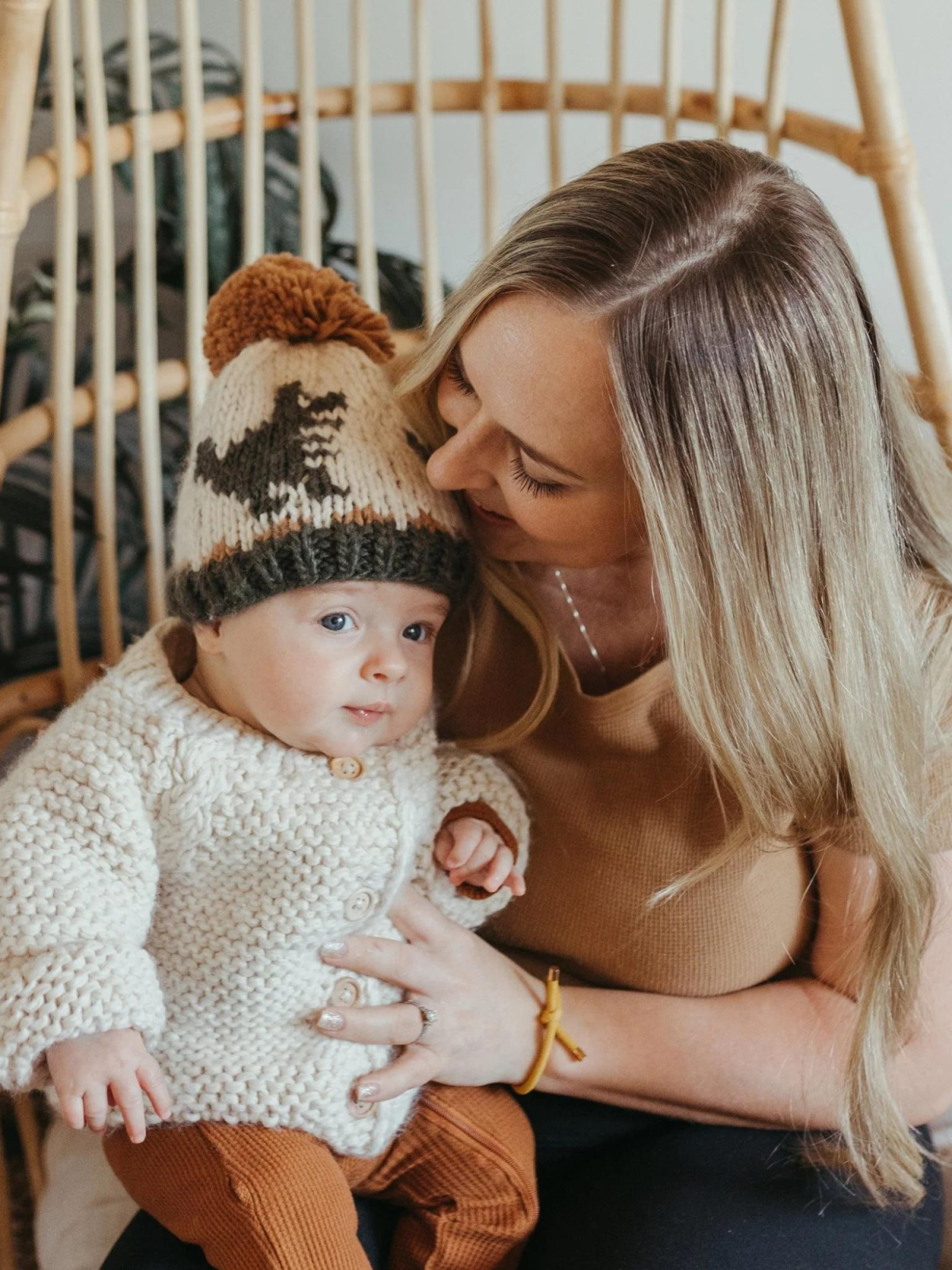 Mother and baby in cozy knitwear, smiling together in a stylish indoor setting.