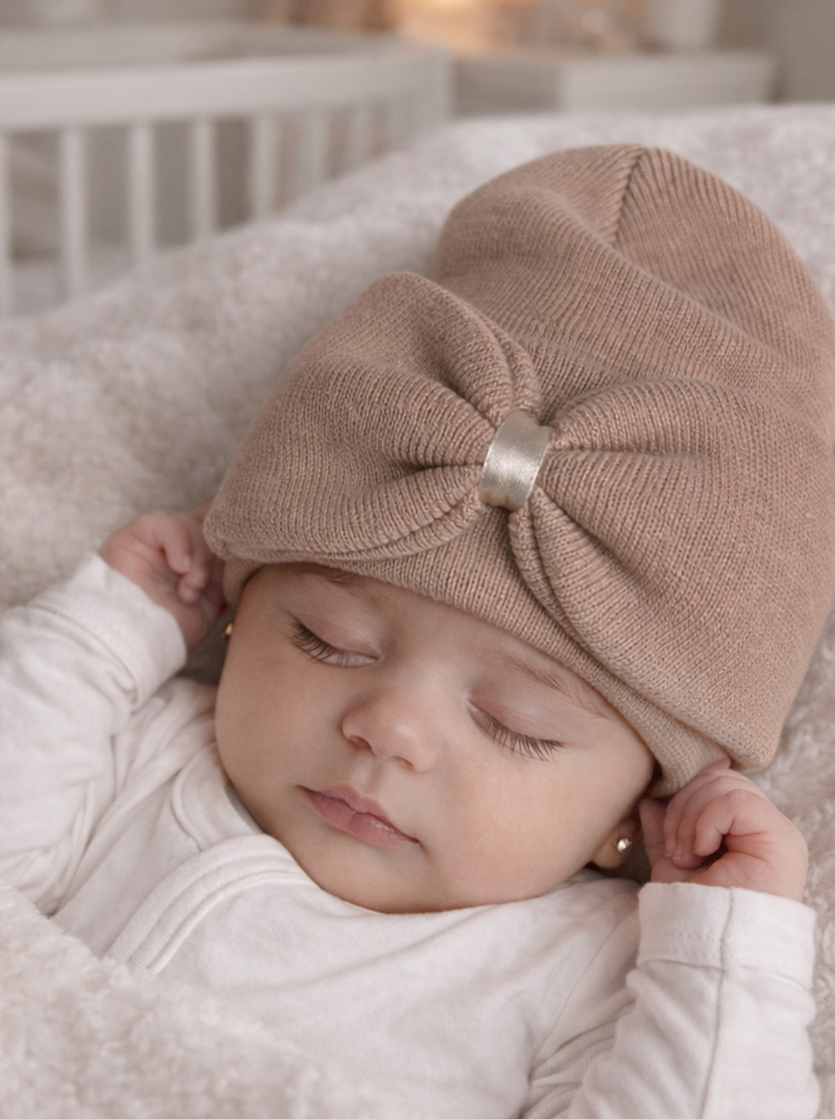 Baby girl peacefully sleeping in a cozy blanket, wearing a knit hat with a bow. Soft, neutral colors.