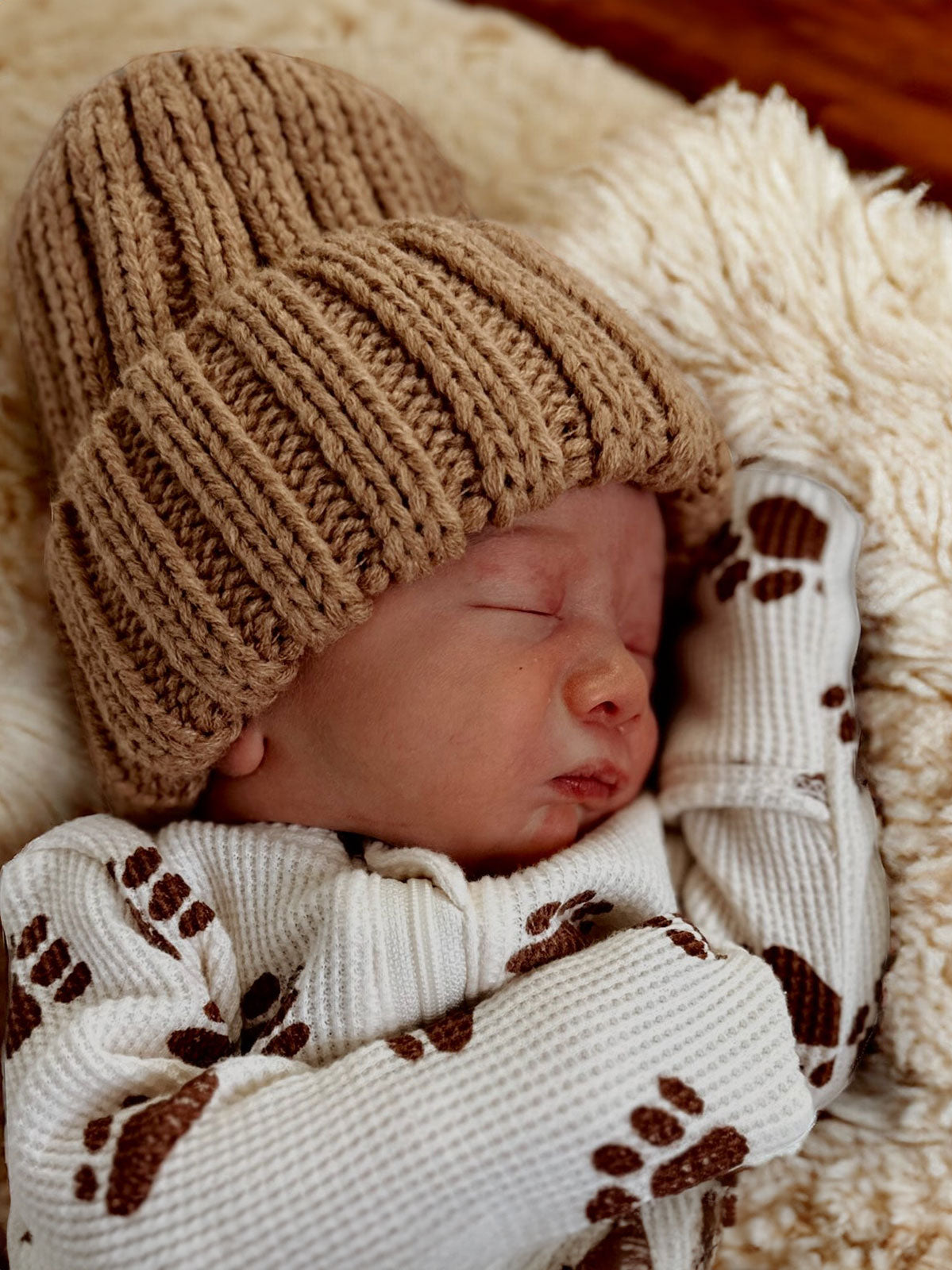 Baby sleeping peacefully in a cozy knit hat and bear-print outfit on a soft blanket.