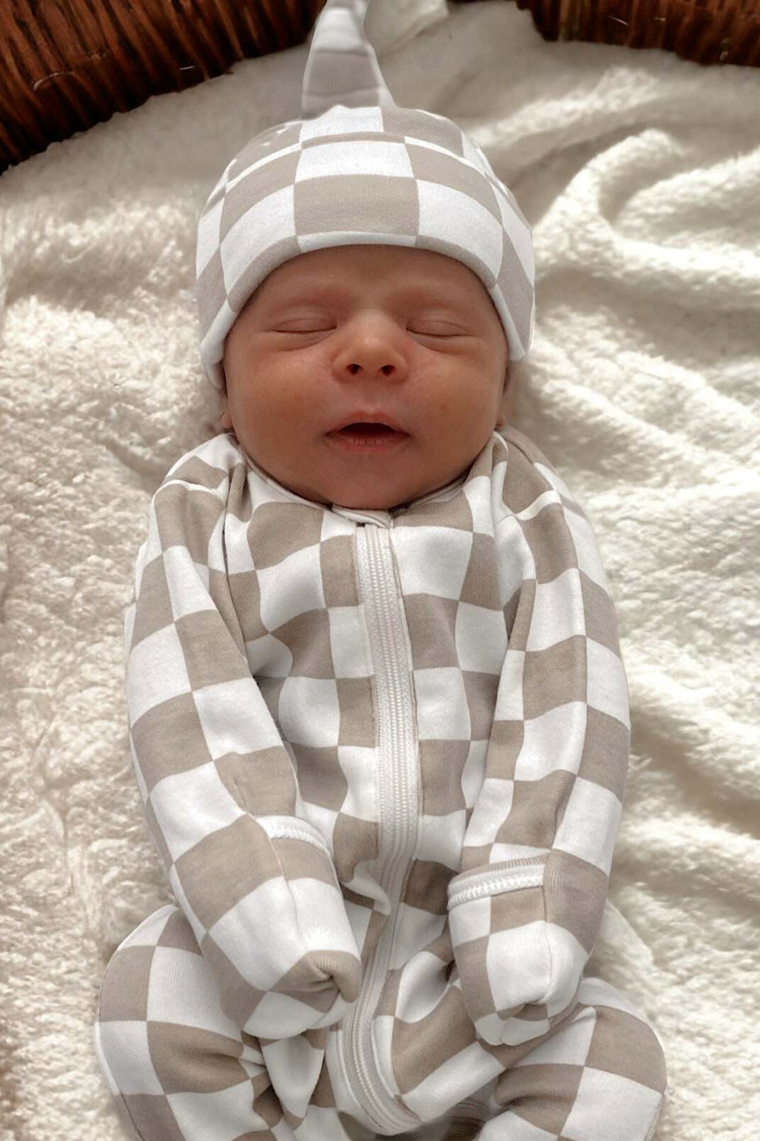 Newborn baby in a beige and white checkered outfit, peacefully sleeping on a soft blanket.