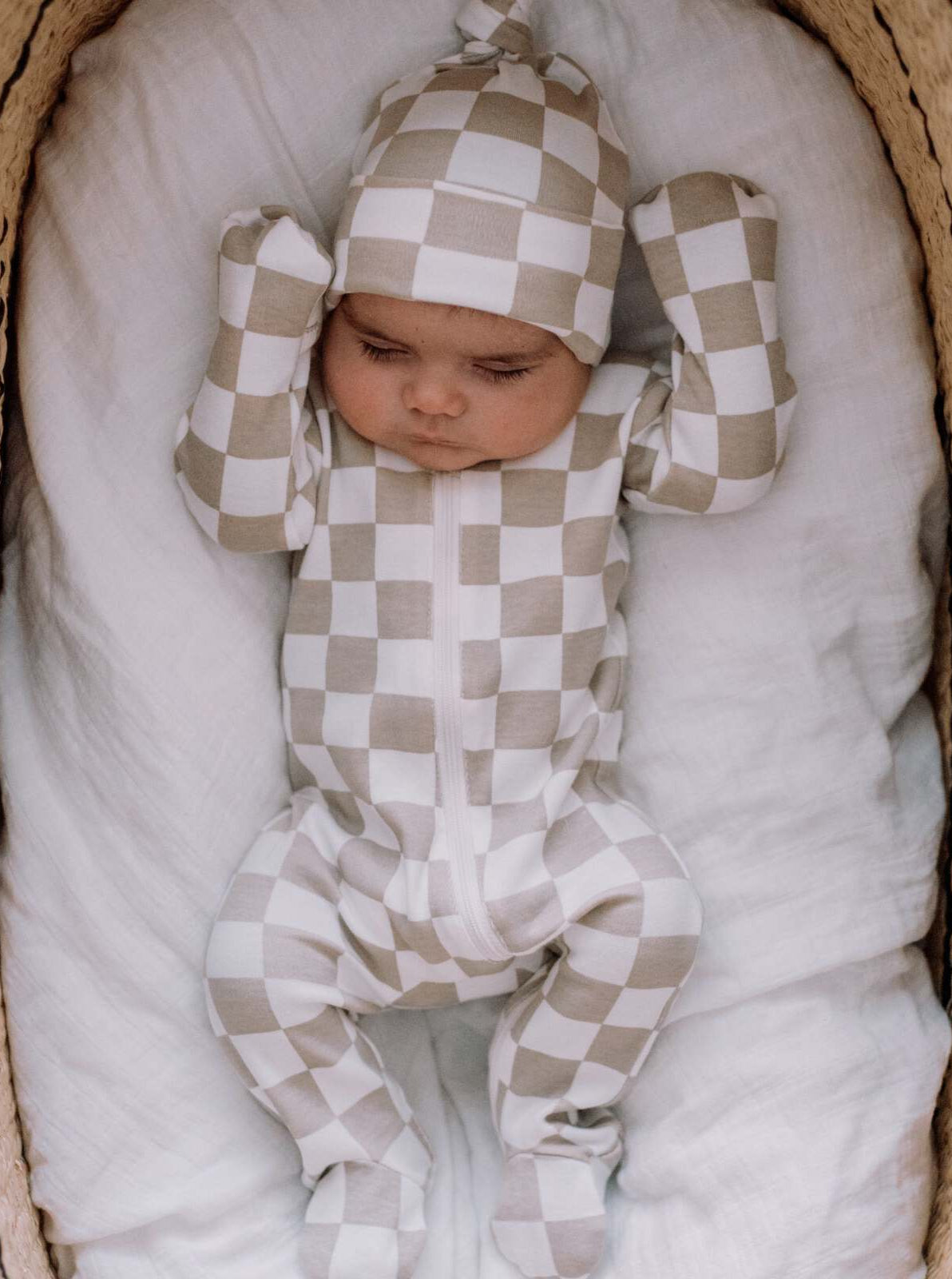 Infant in a beige and white checkered outfit lying on a soft blanket, looking peacefully asleep.