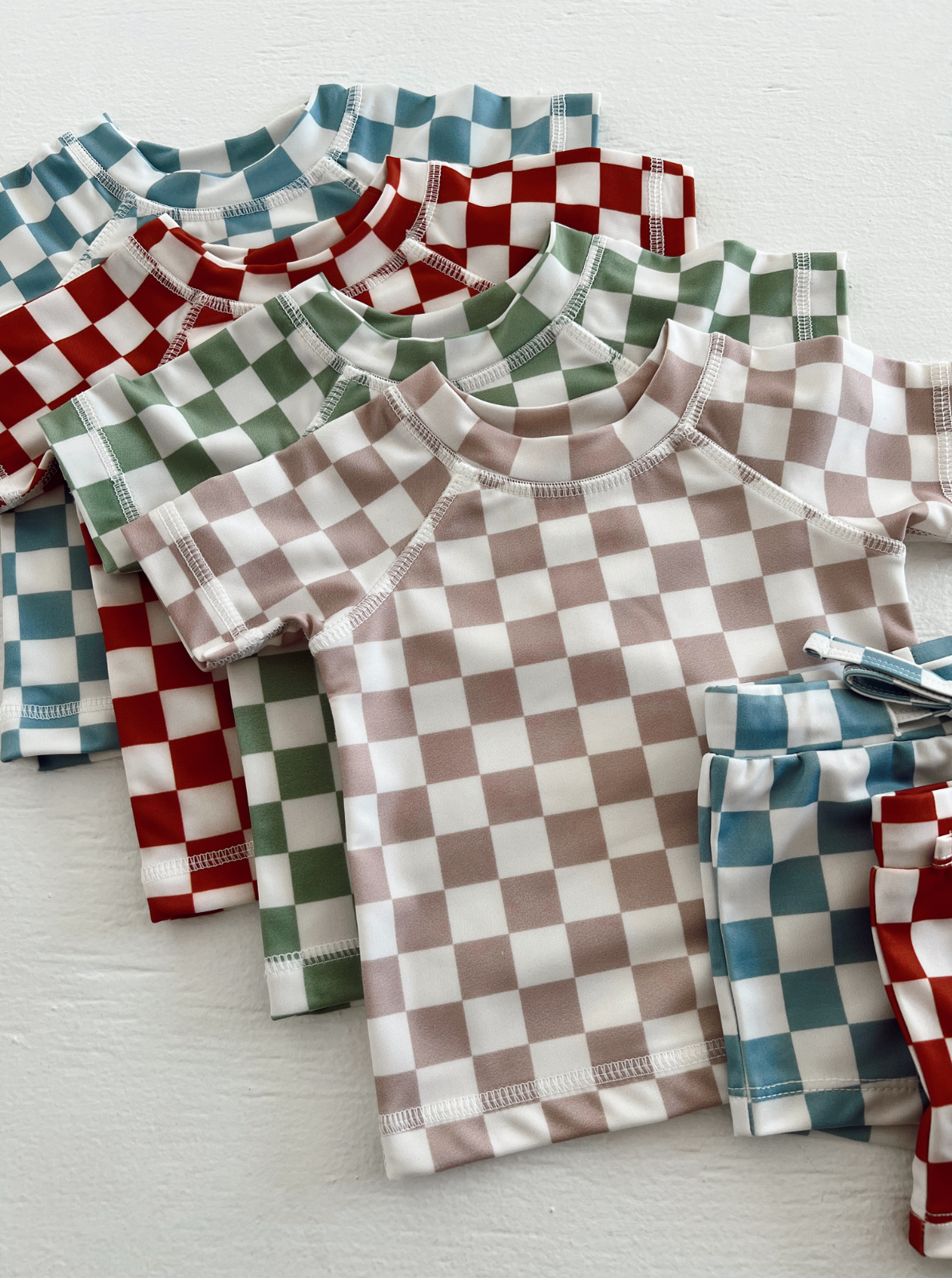 Colorful checkered kids' shirts and shorts stacked together on a white surface.