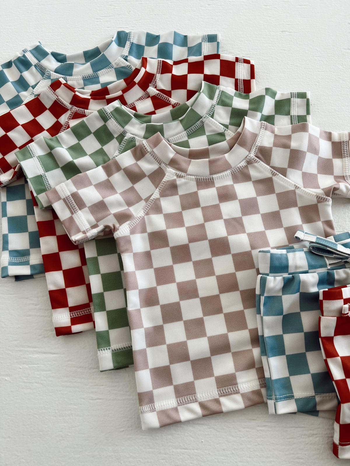 Colorful checkered kids' shirts and shorts stacked together on a white surface.
