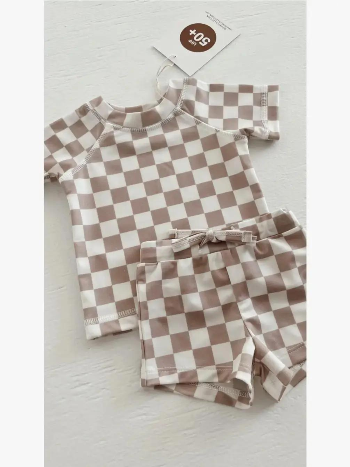 Brown and white checkered toddler swimsuit set with a short-sleeve top and matching shorts.