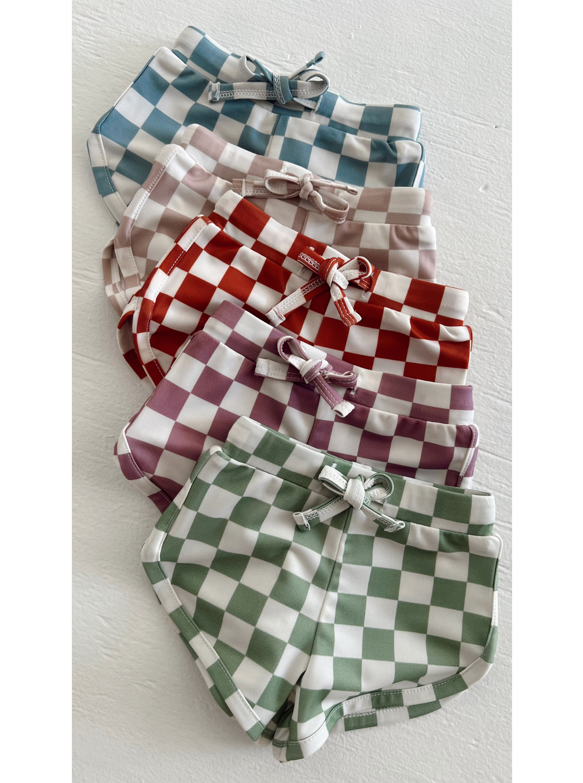 Assorted checkered shorts in blue, pink, red, maroon, and green arranged on a white background.