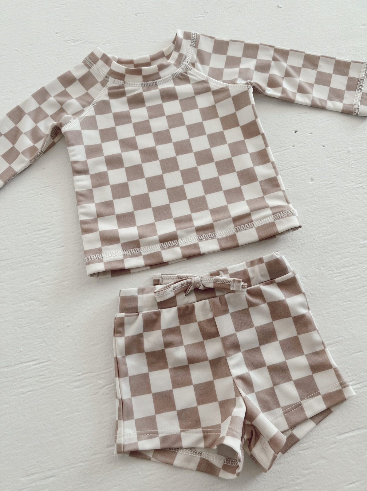 Brown and white checkered toddler swim shirt and shorts set on a light surface.