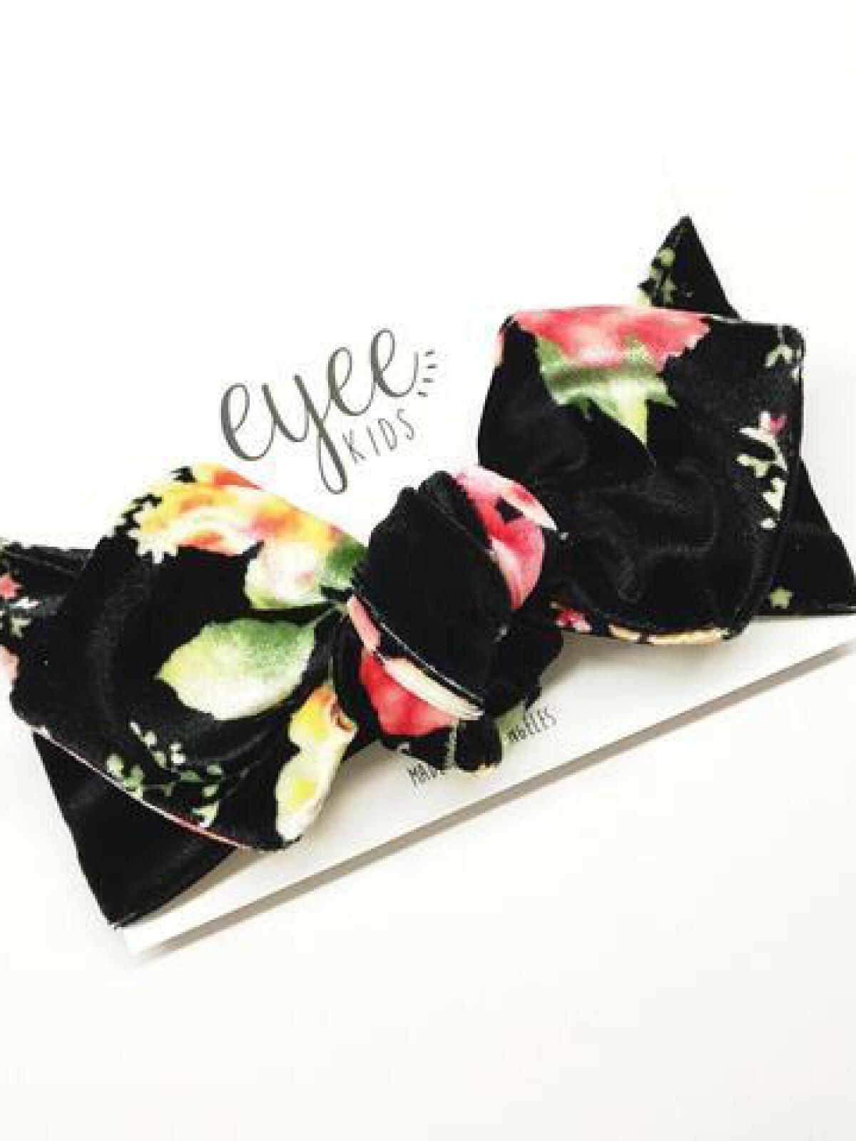 Black floral headband with a large bow on a branded card. Ideal accessory for kids.
