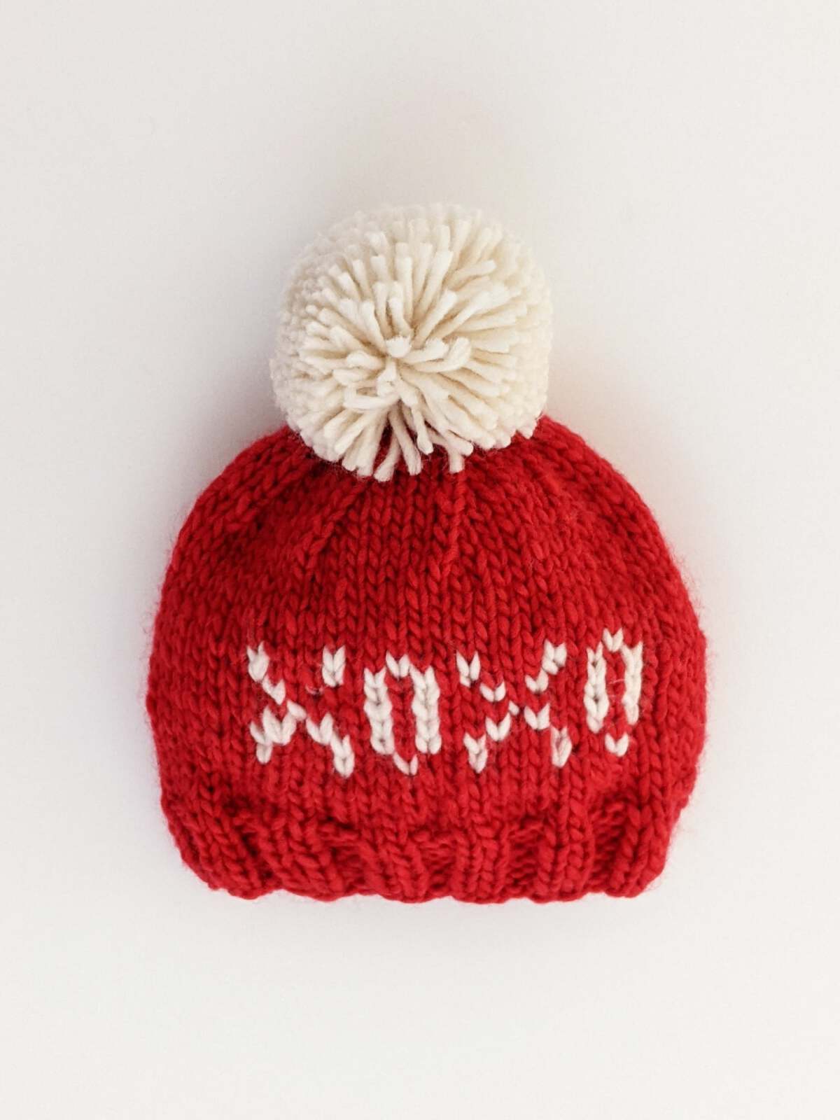 Red knitted hat with a white pom-pom, featuring the word "xoxo" in white yarn.