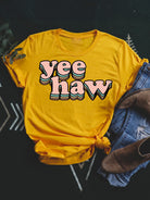 Yellow t-shirt with "yeehaw" in bold, playful letters, styled with jeans and boots on a dark background.