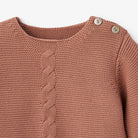 Brown knit sweater with a cable pattern and decorative buttons at the shoulder.