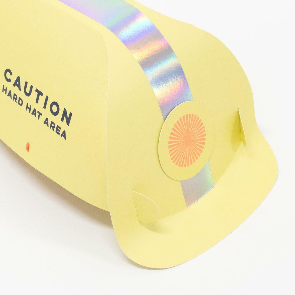 Yellow hard hat with a rainbow stripe and "Caution Hard Hat Area" text.