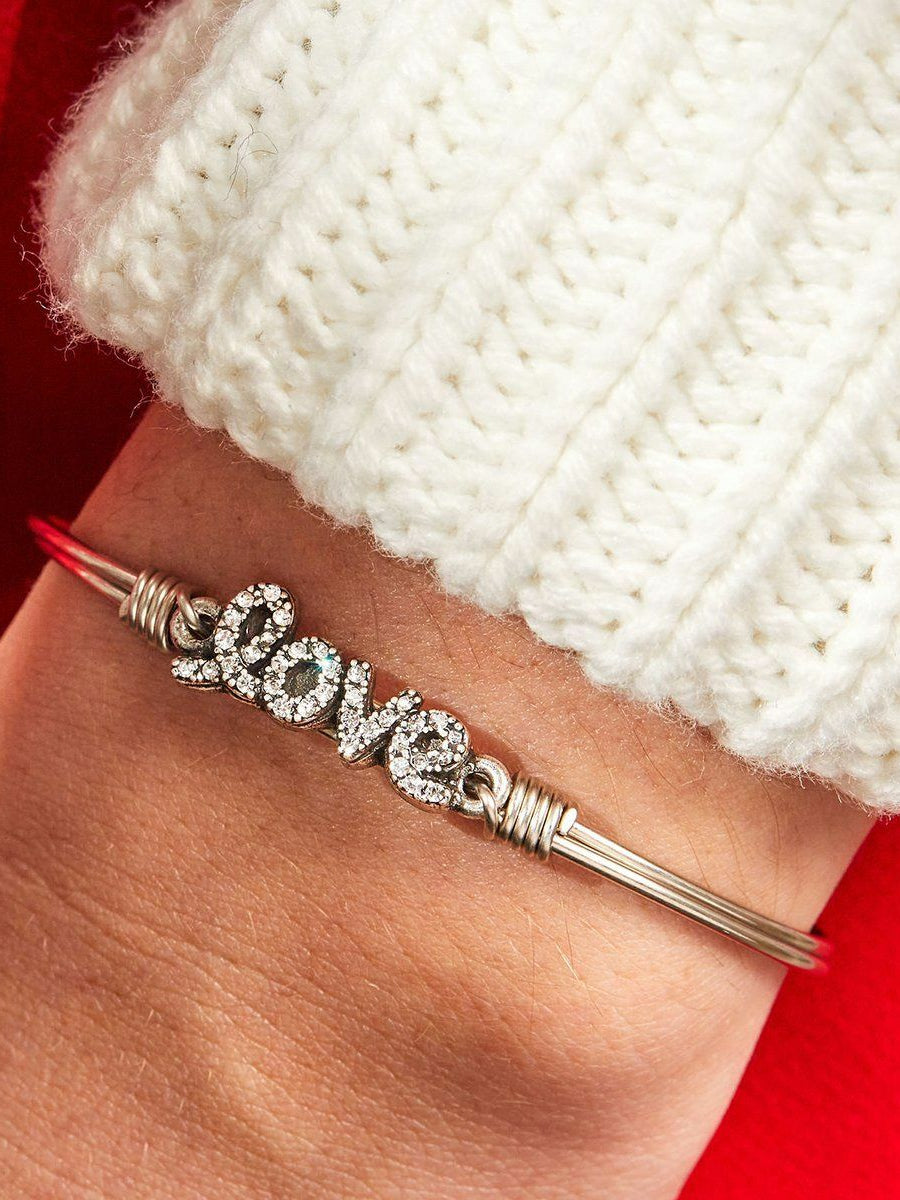 Silver bracelet with the word "love" adorned with sparkling stones, resting on a wrist in a cozy white sweater.