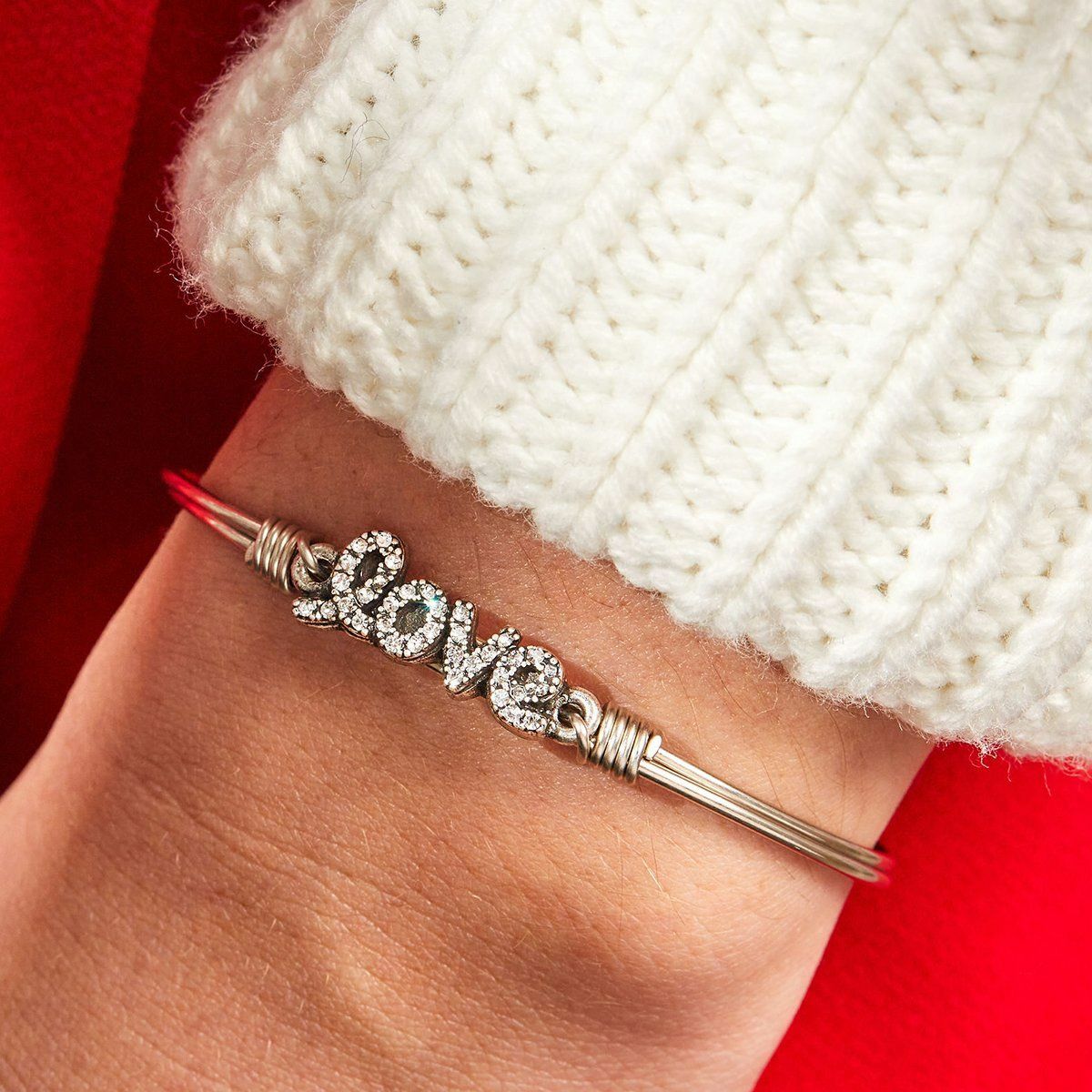 Silver bracelet with the word "love" adorned with sparkling stones, resting on a wrist in a cozy white sweater.