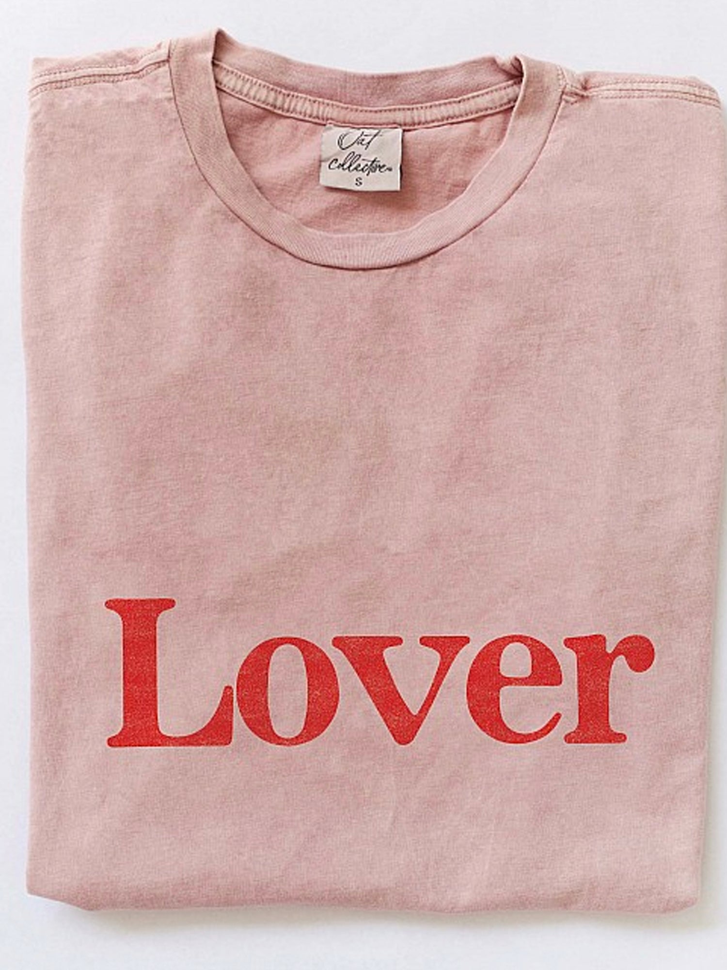 Pink t-shirt folded, featuring the word "Lover" in bold red letters.