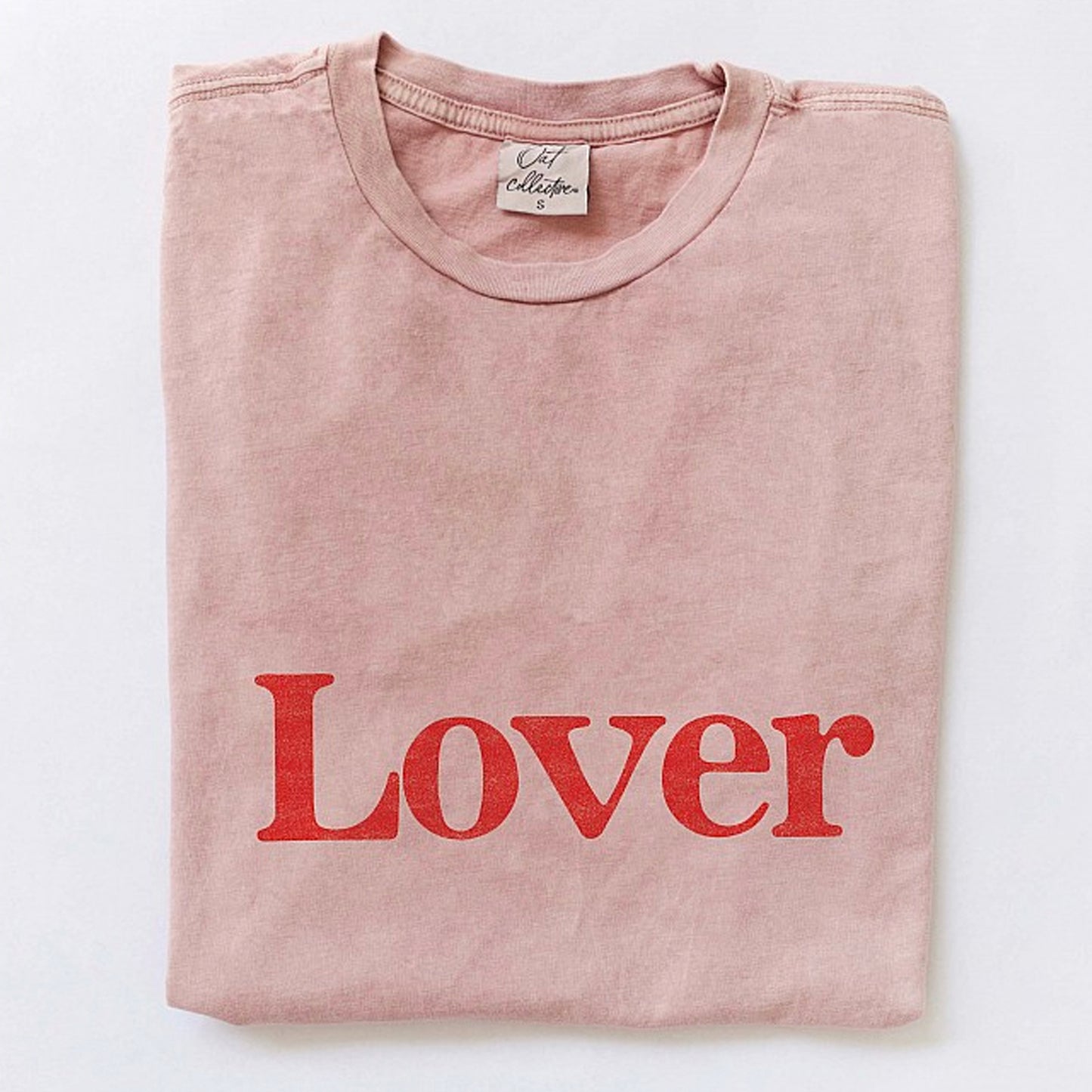 Pink t-shirt folded, featuring the word "Lover" in bold red letters.
