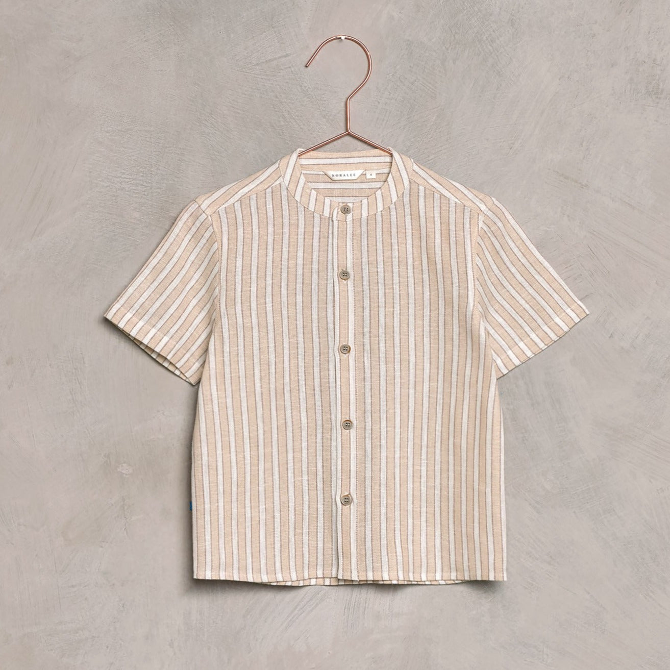 Short-sleeve striped linen shirt with a round collar, hanging on a copper hanger against a textured background.
