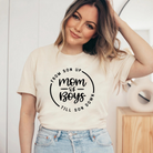 Woman wearing a light-colored t-shirt with "Mom of Boys" graphic, smiling in a modern interior.