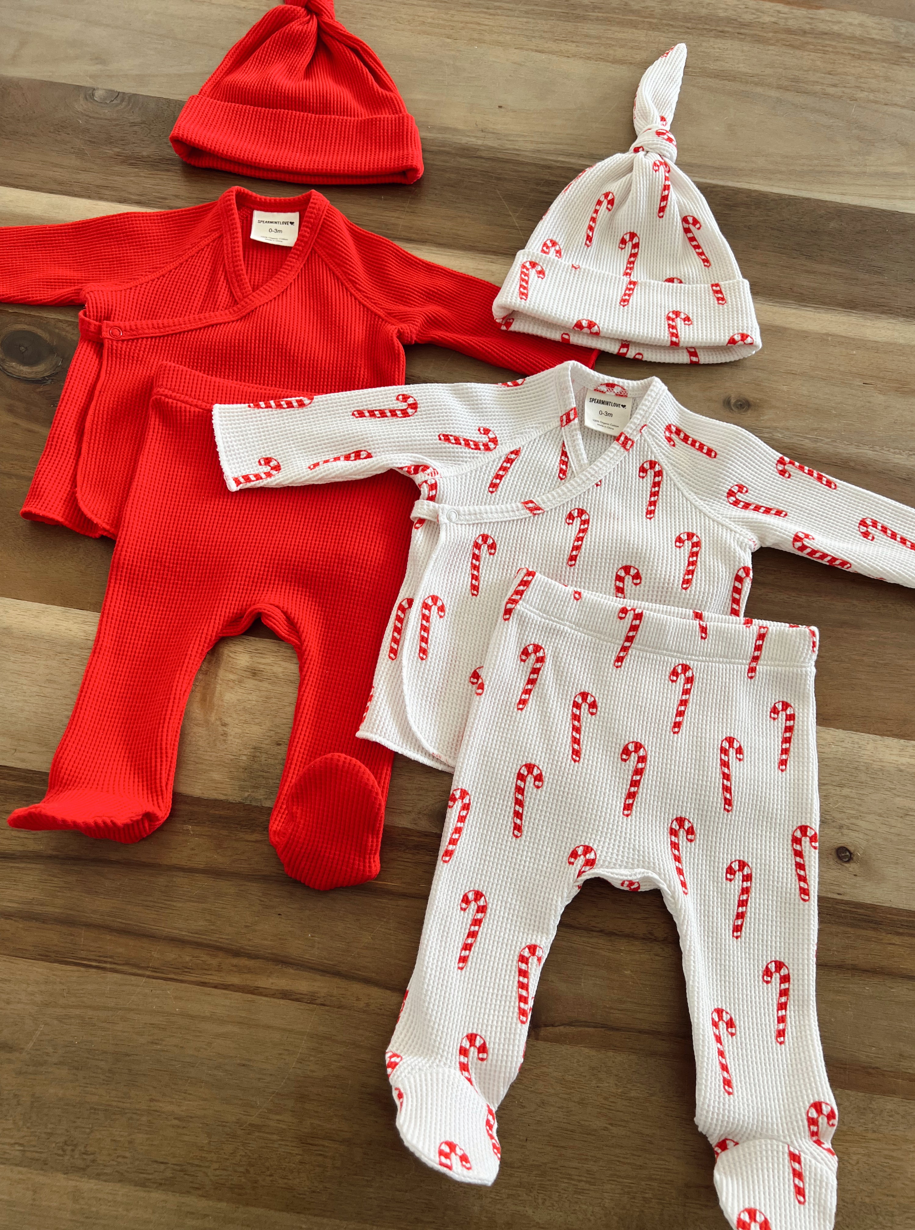 Bundle of baby clothing: red outfits and white pajamas with candy cane patterns, plus a matching hat.