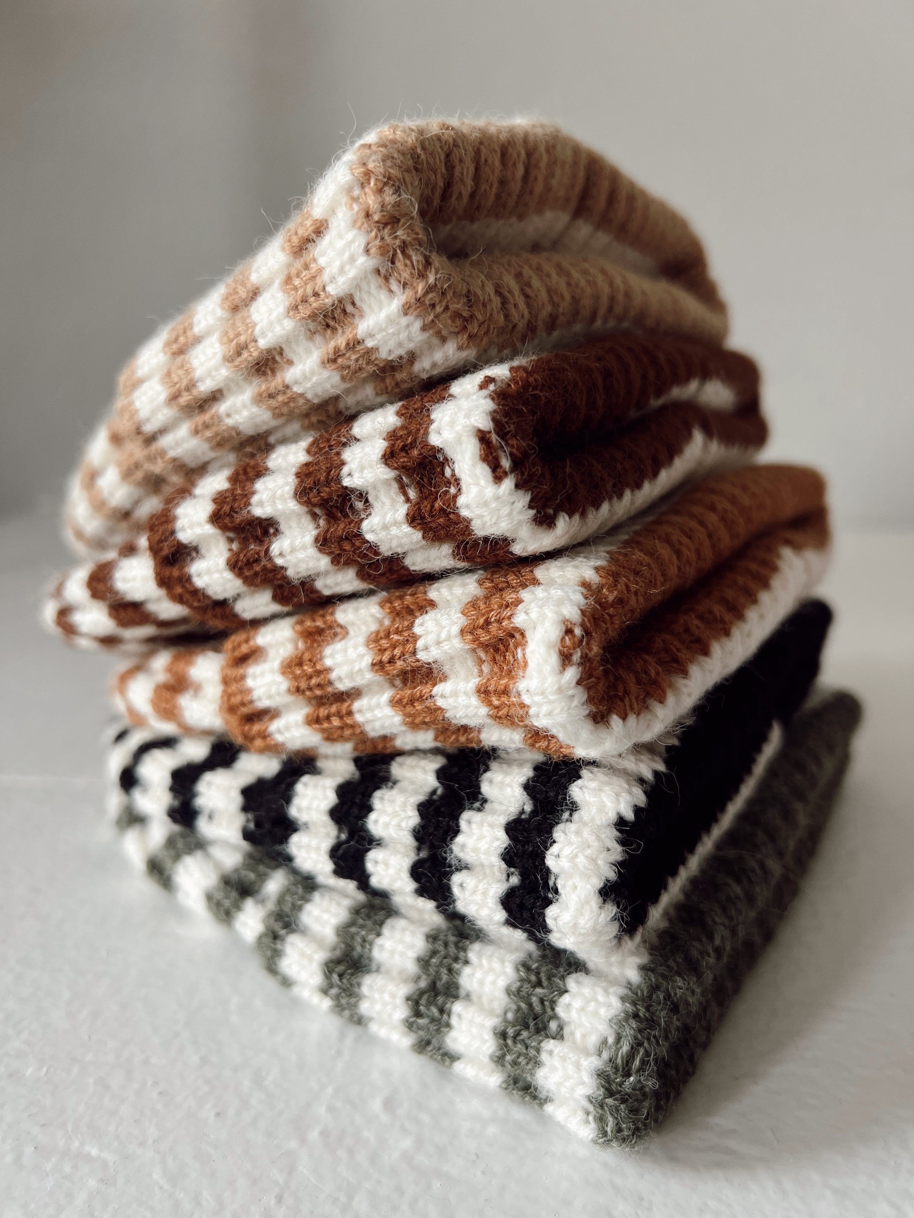 Stack of cozy striped knit socks in warm tones of brown, cream, black, and green on a white surface.
