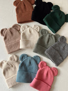 A collection of colorful bear-ear beanies arranged on a light background.