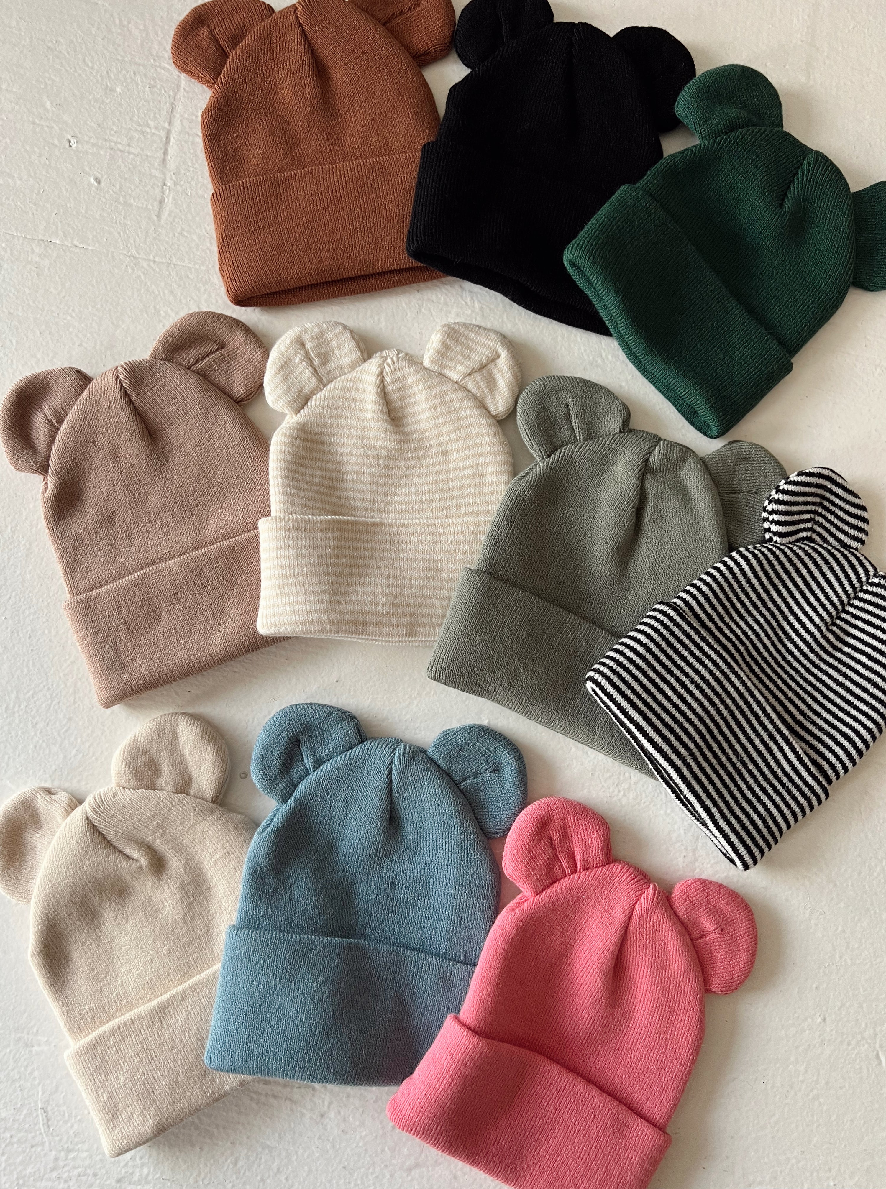 Colorful bear-eared beanies arranged on a flat surface, featuring pastel and neutral tones.
