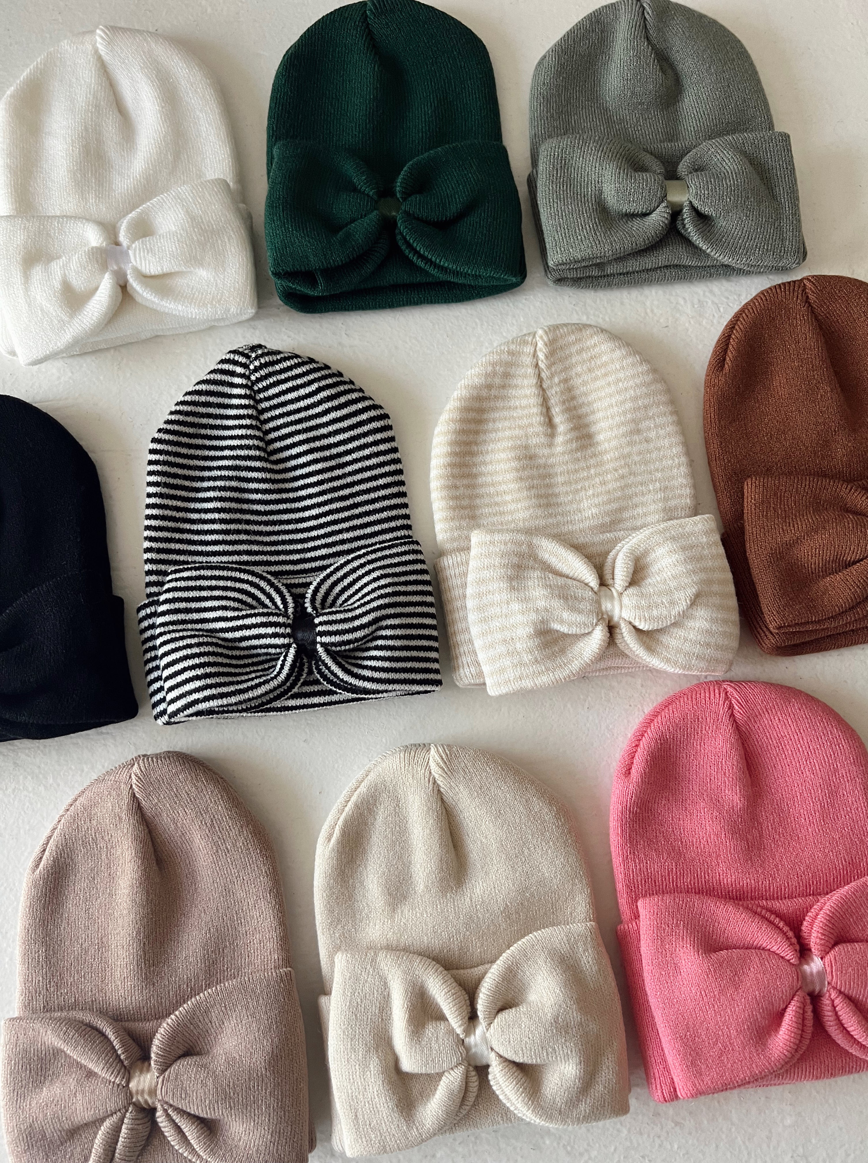 A collection of colorful beanie hats with bows, arranged in rows on a white surface.