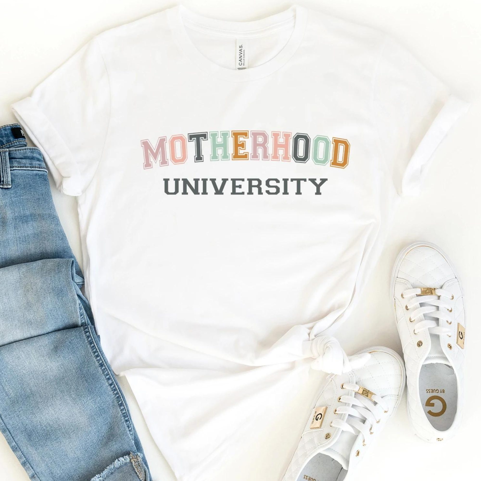 White t-shirt with "Motherhood University" print, paired with light jeans and white sneakers.
